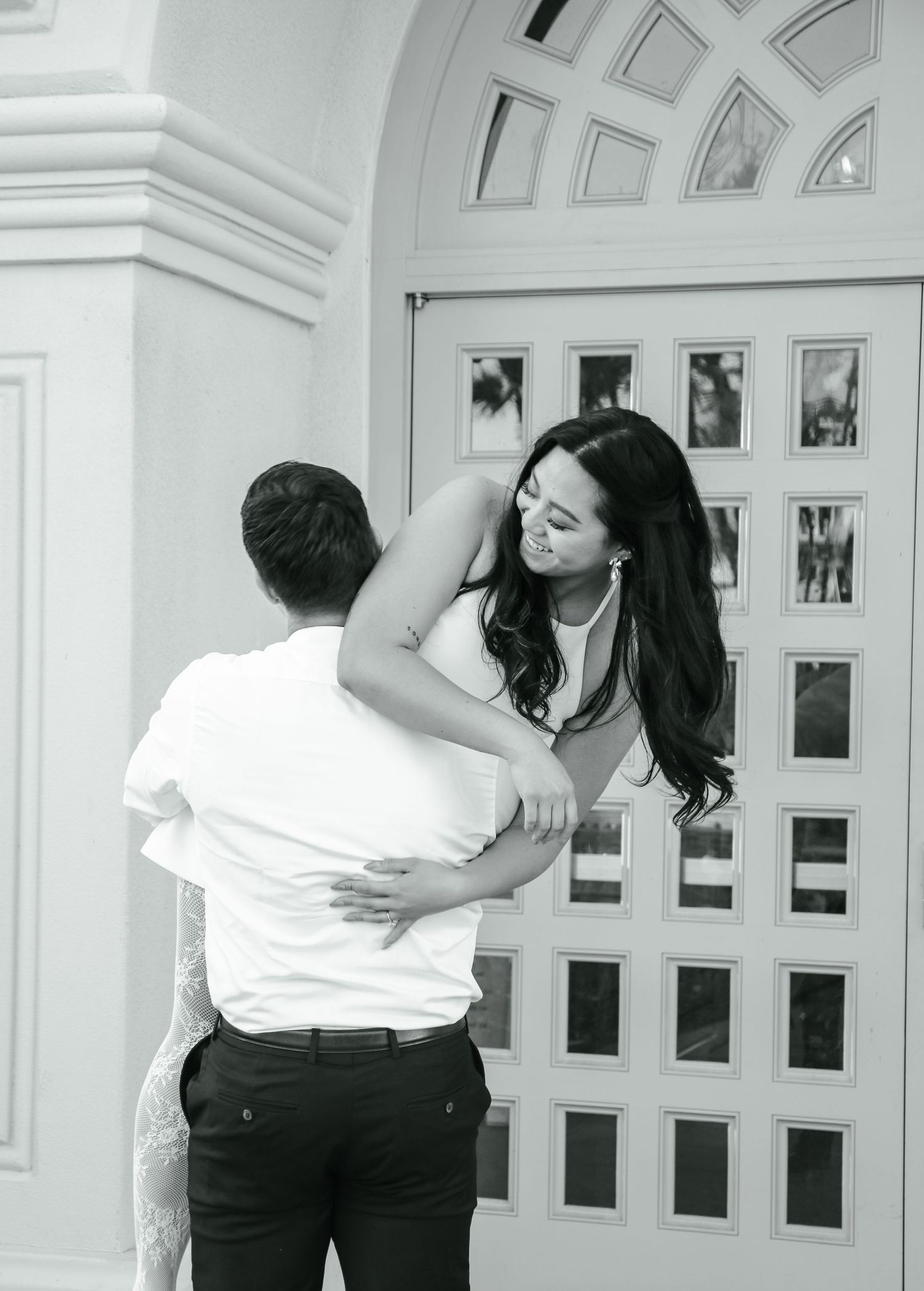 Black and white photo of a romantic embrace in front of an architectural doorway.