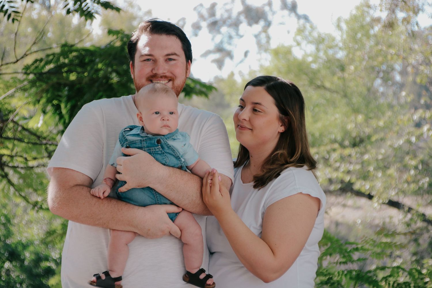 A candid family photo showing joyful interaction between parents and baby in a natural outdoor setting.