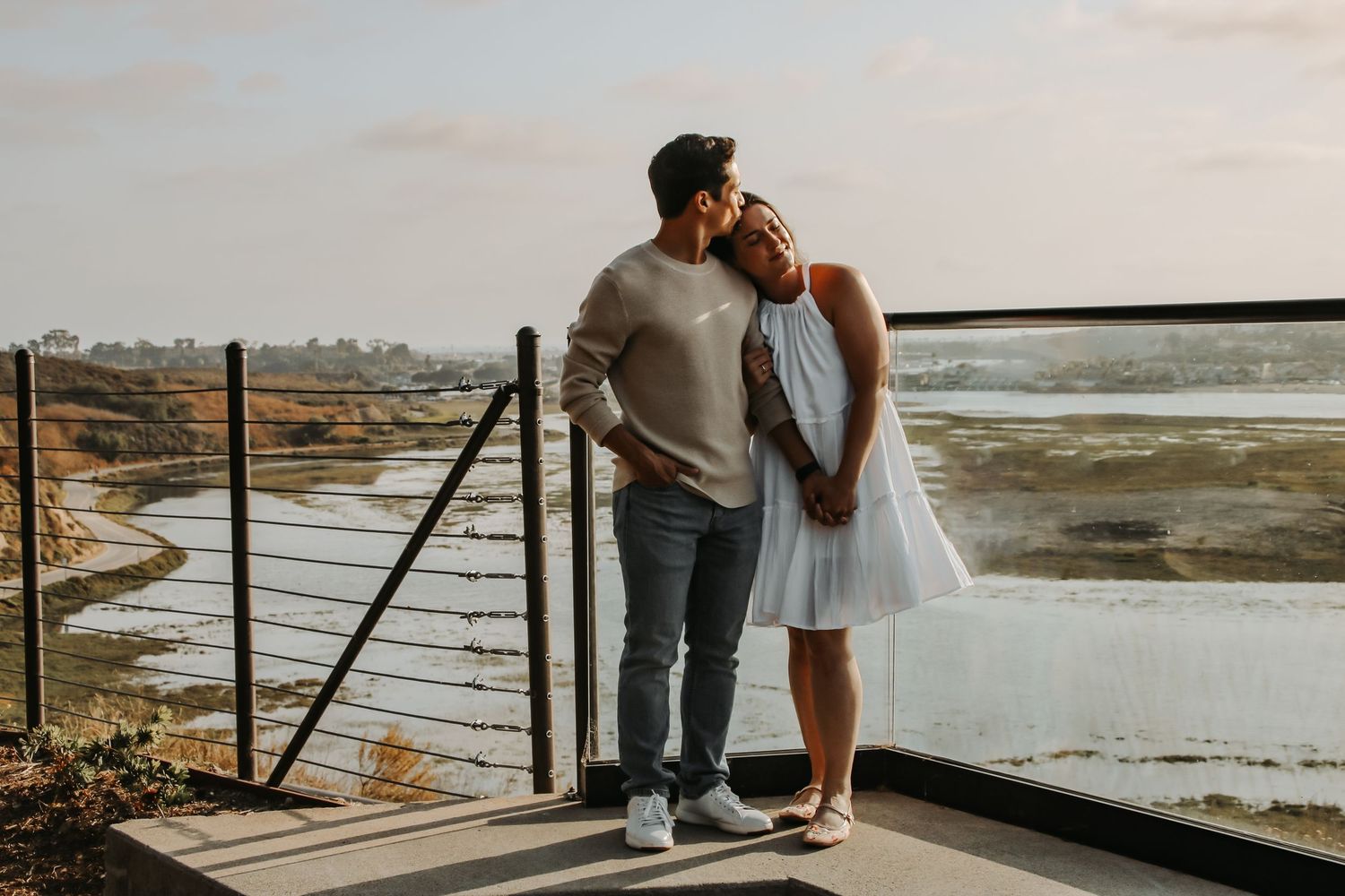 A tender moment between a couple on a scenic overlook during sunset, with wetlands in the background.