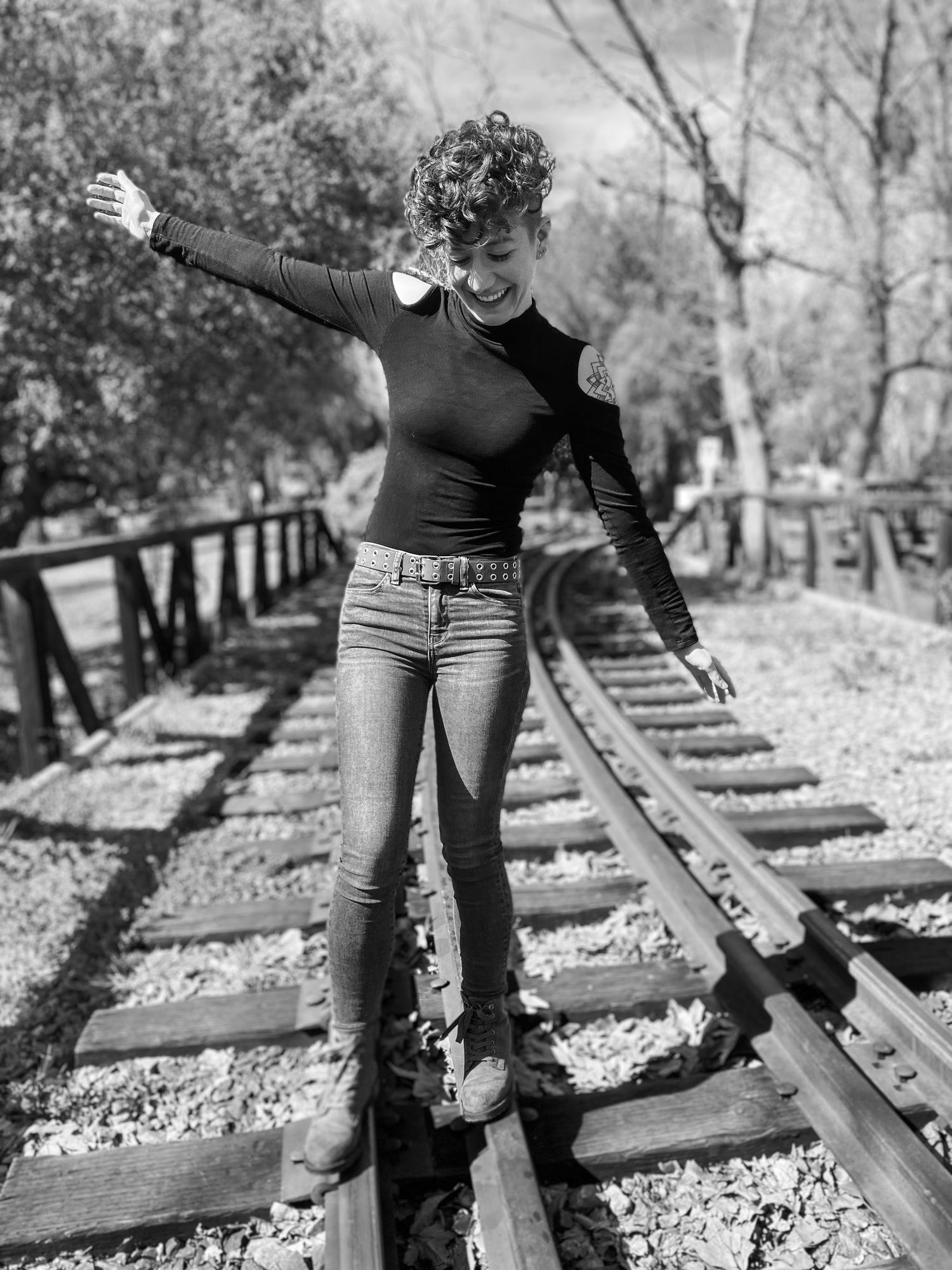 Black and white photo of legs standing on railroad tracks in nature.