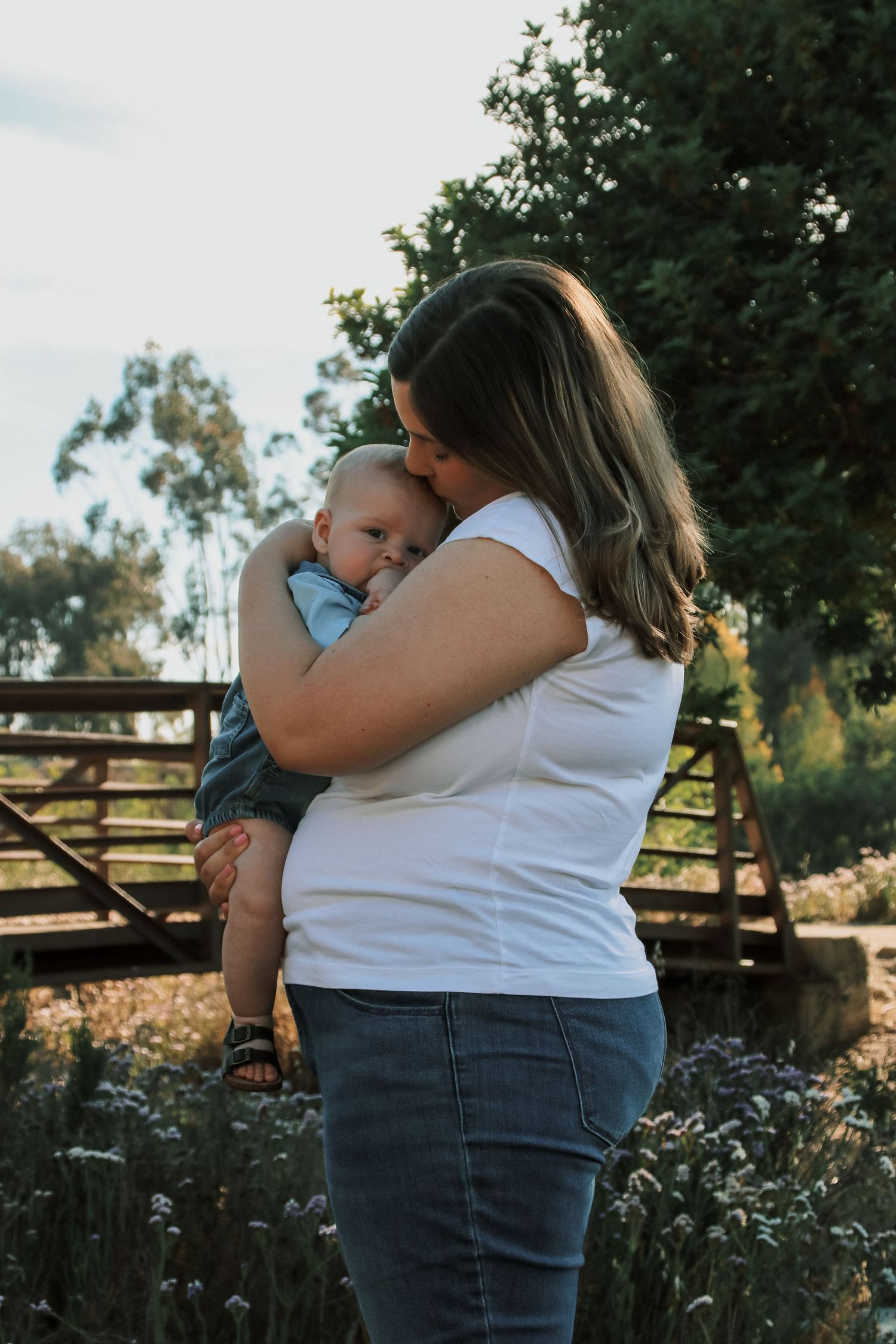 Mother cradling baby during sunset photoshoot in outdoor garden setting.