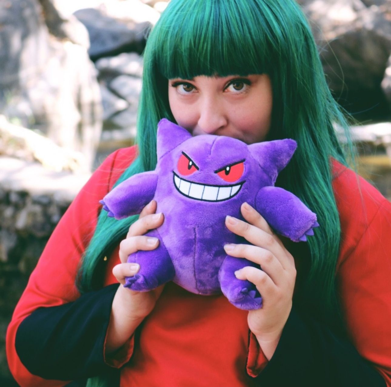 Person with green hair playfully interacting with purple Pokemon plush toy.