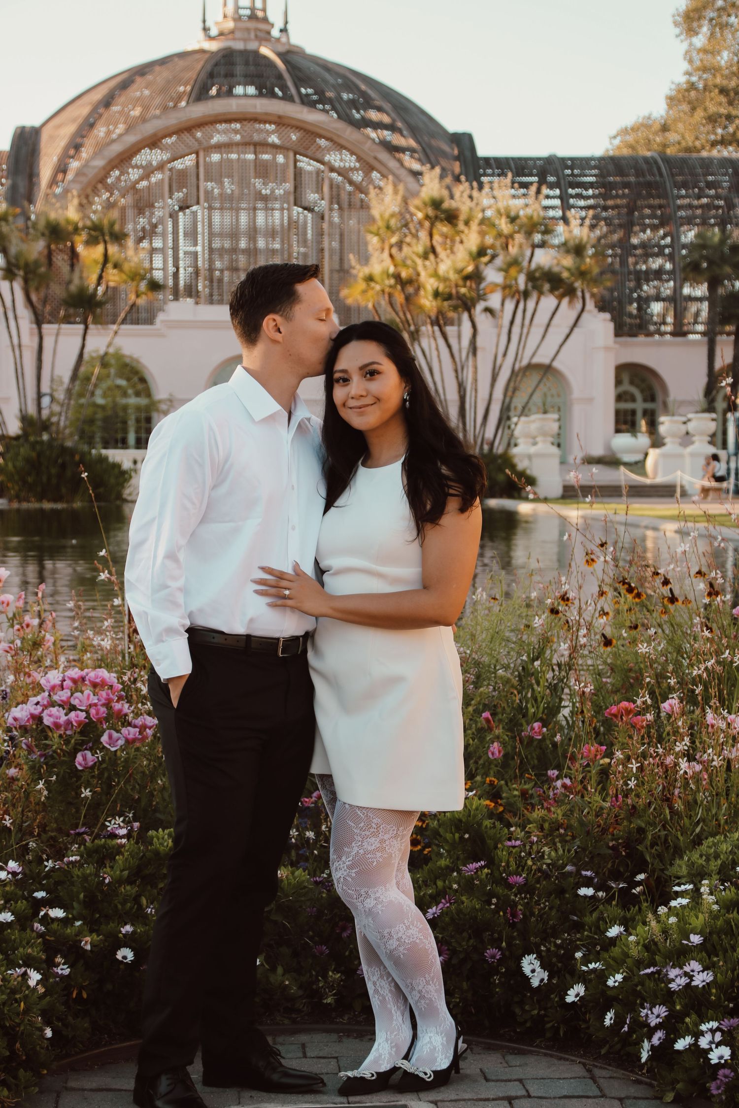 A couple poses for romantic photos in a garden setting with beautiful flowers and architecture.