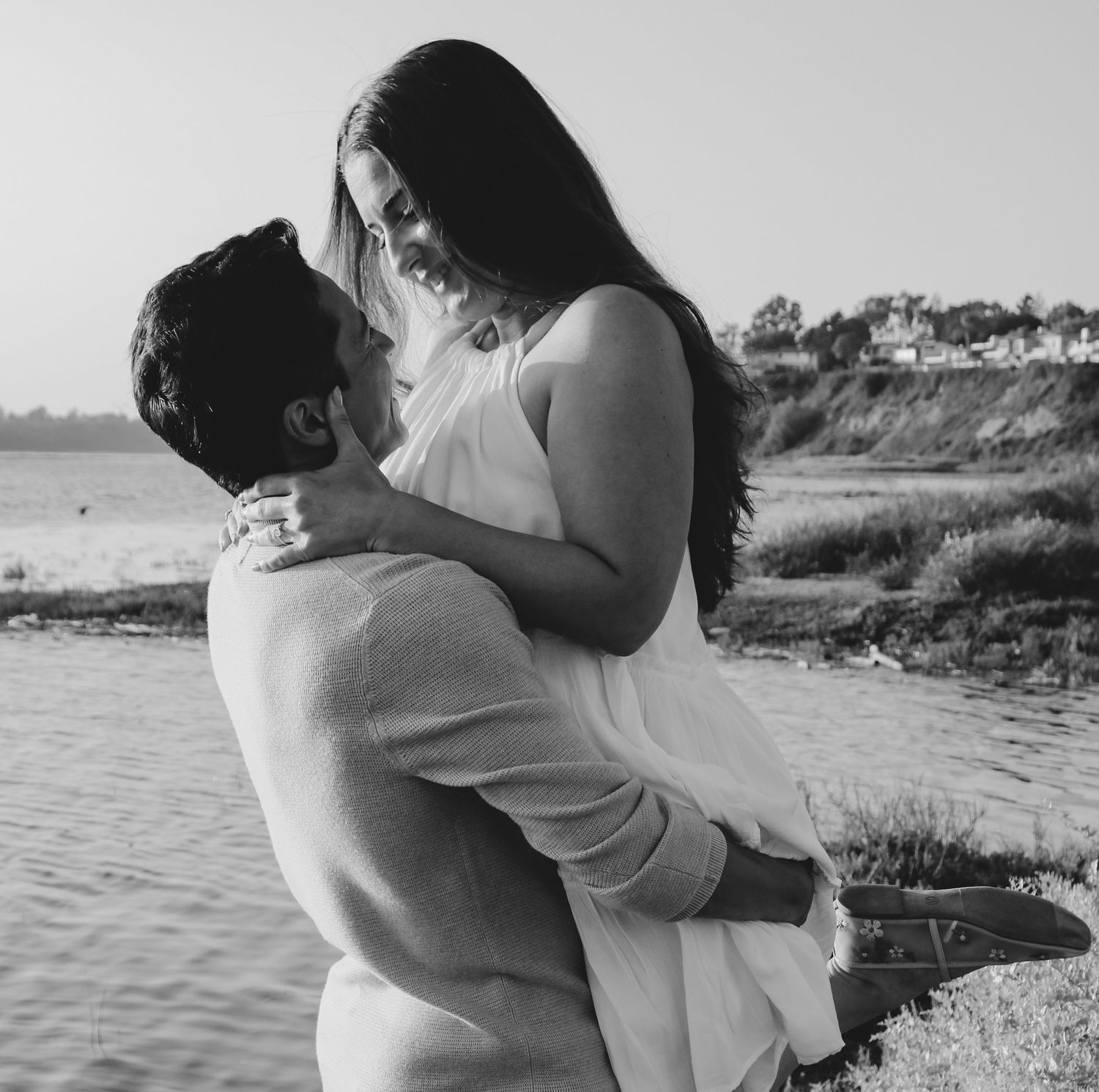 A black and white photo of a couple sharing an intimate moment by the water.