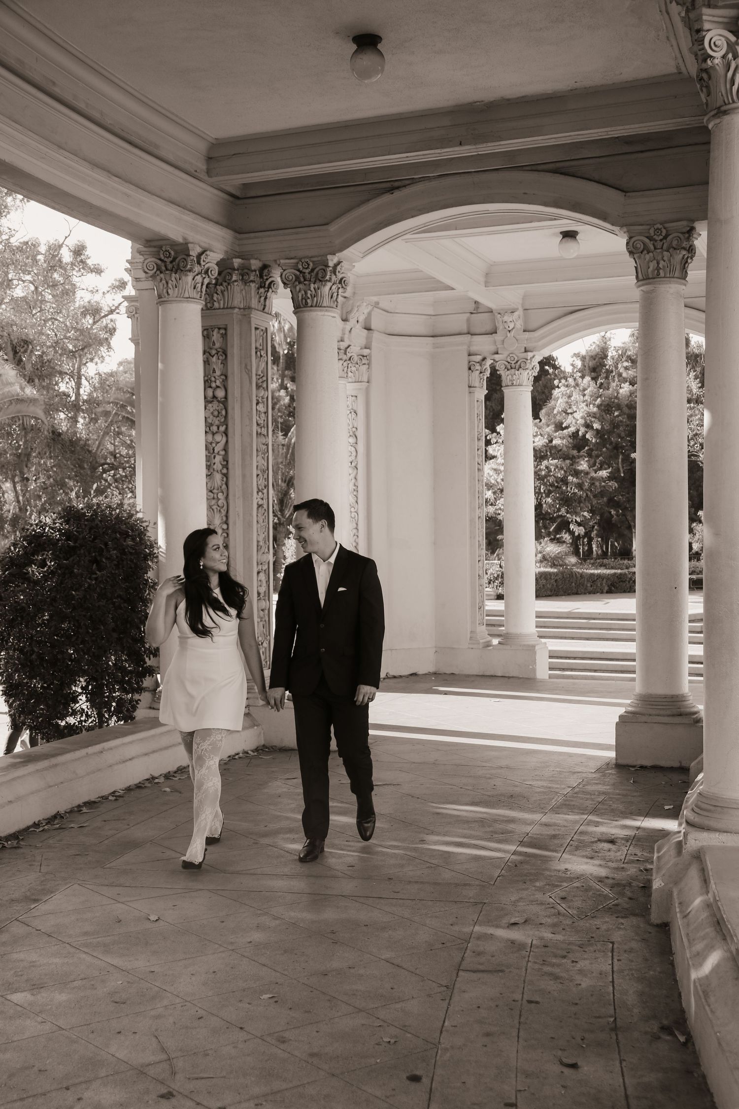 Couple walking together under ornate classical columned archway in black and white.
