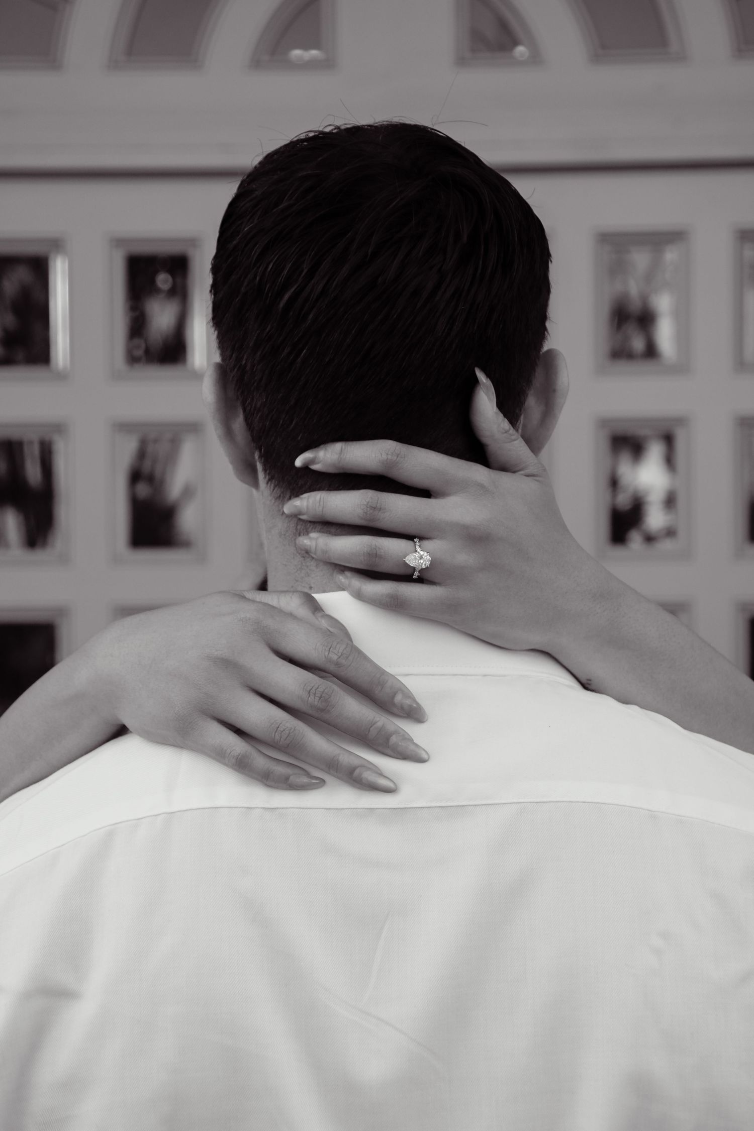 Close-up of hands gently resting on shoulders in black and white.