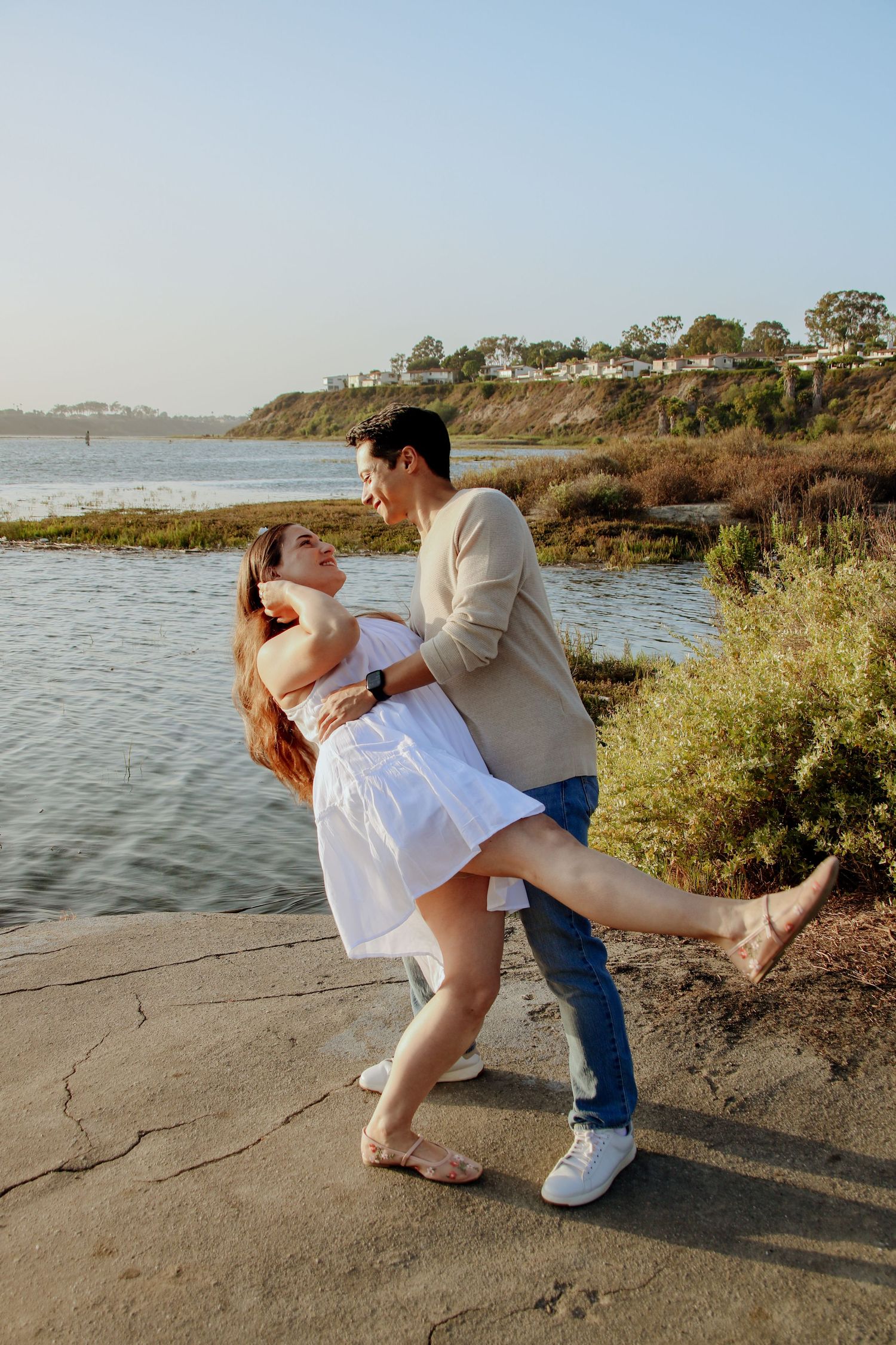 A couple shares a romantic dance pose by the waterfront at sunset.