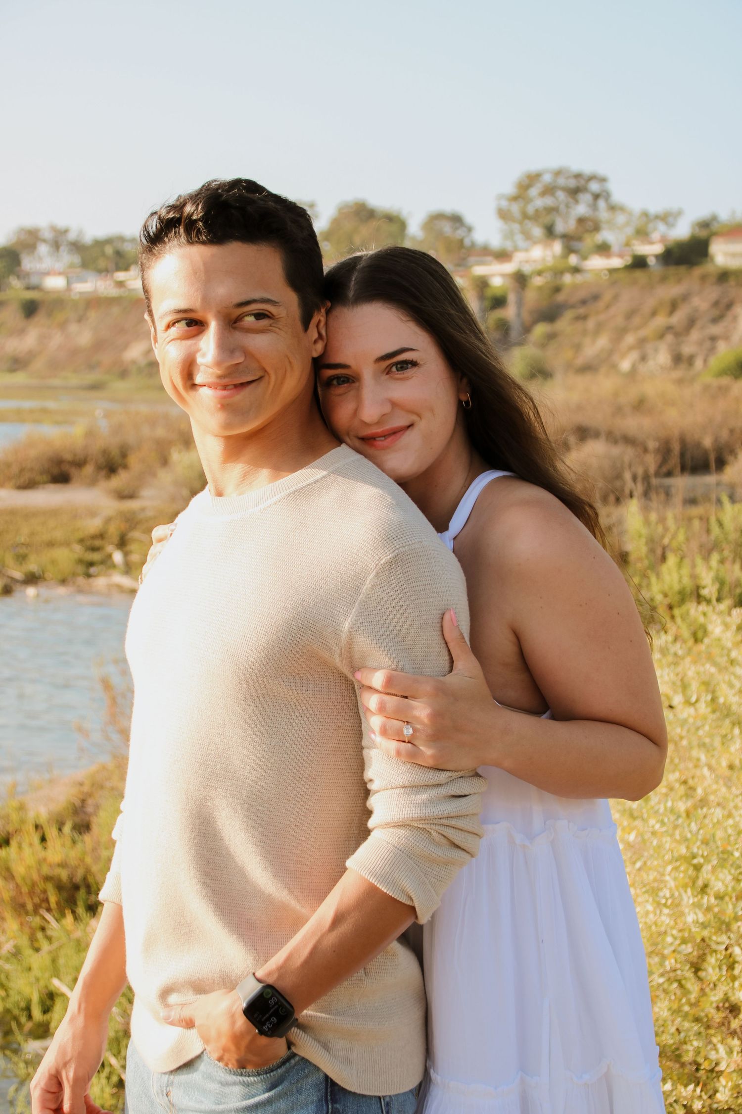 Candid outdoor portrait of couple standing close together by scenic waterway.