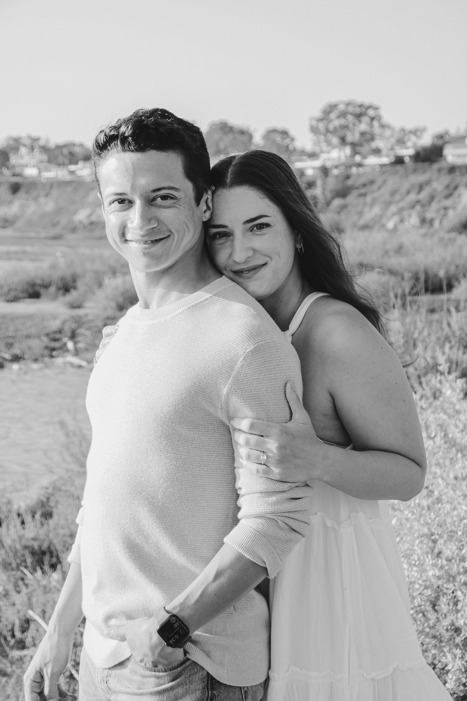 Black and white photo of a joyful couple posing together near coastal cliffs.