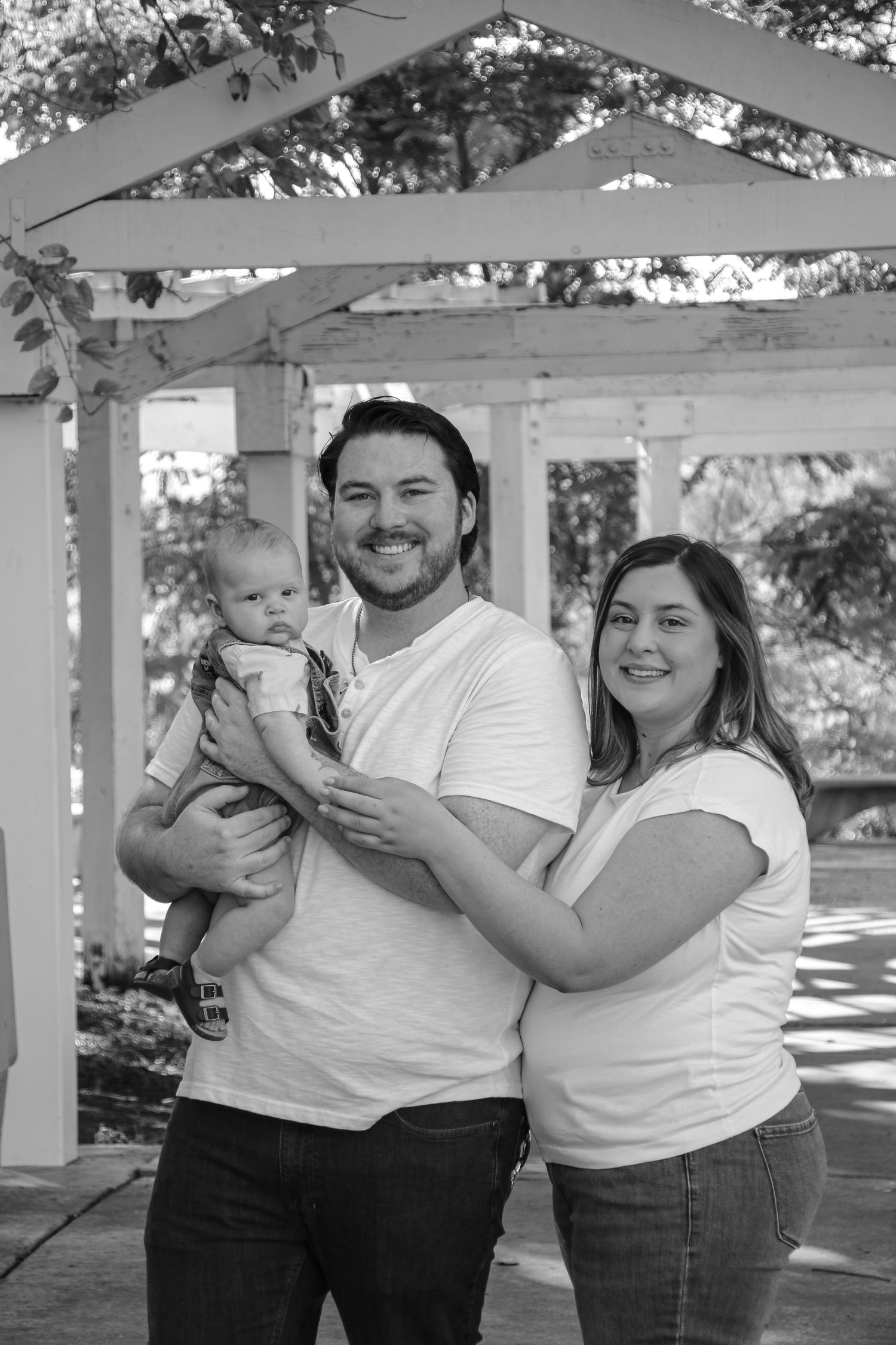 Black and white portrait of family with infant under white pergola structure.