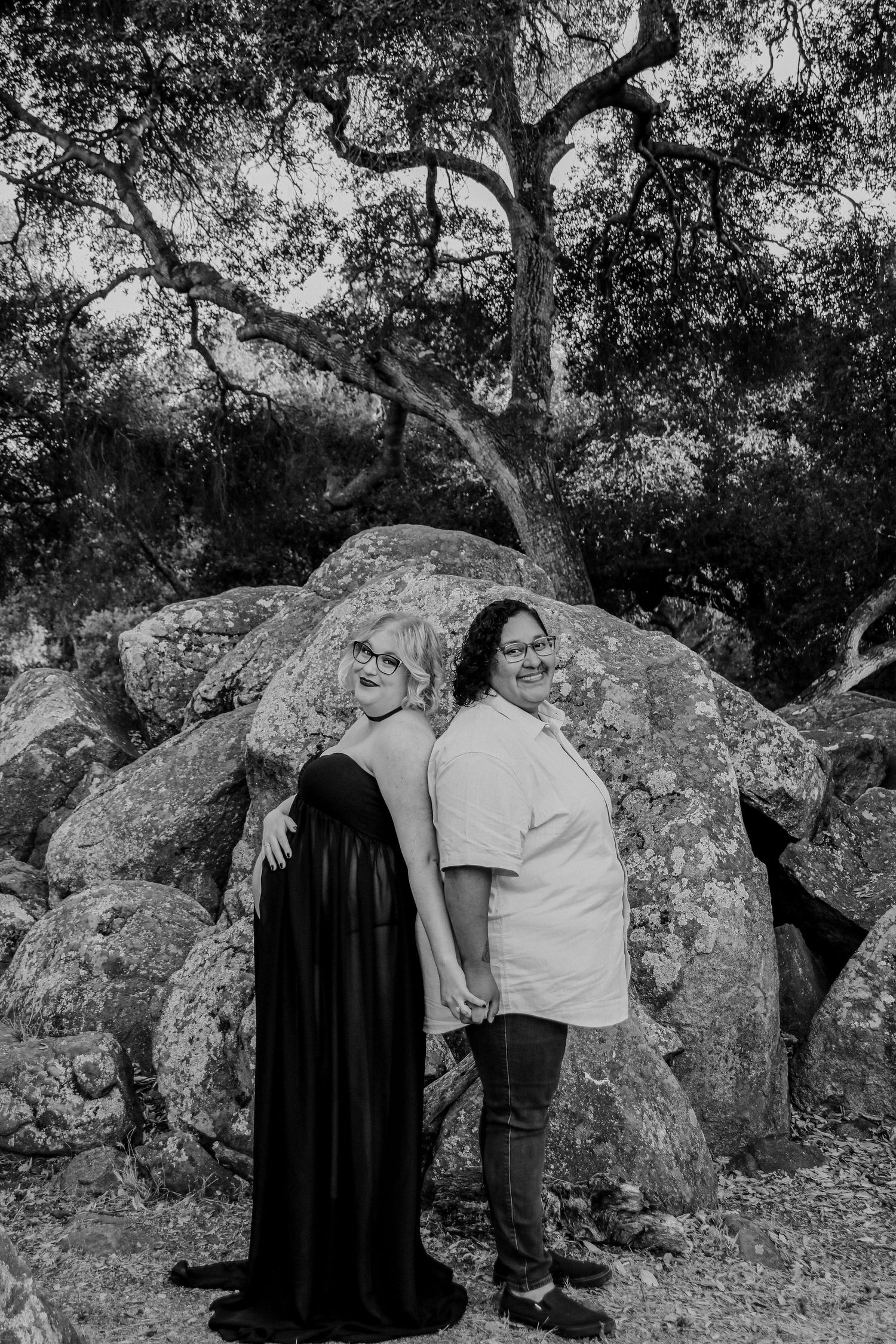 Two people share an intimate moment against large rock formations and twisted tree branches.