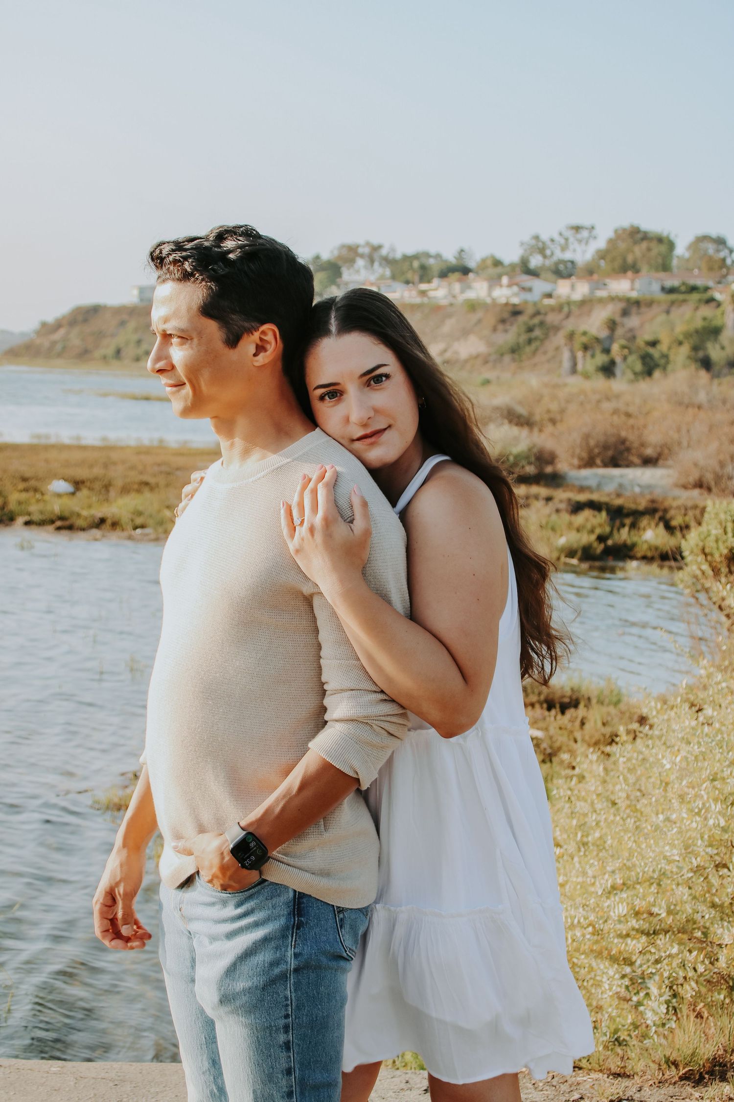 Couple in casual attire sharing intimate moments by waterfront during golden hour.