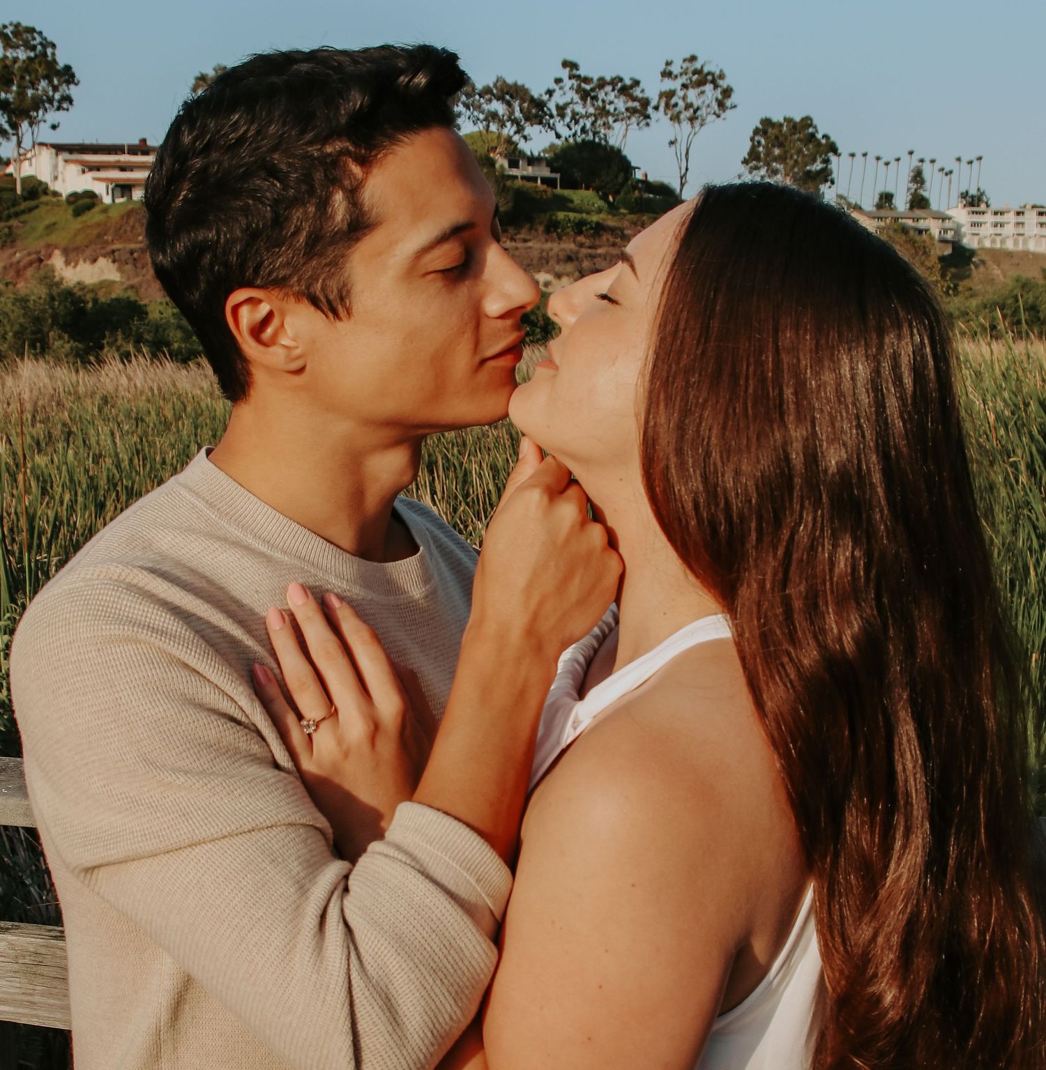 Couple in warm sunlight embracing tenderly against a natural landscape backdrop.