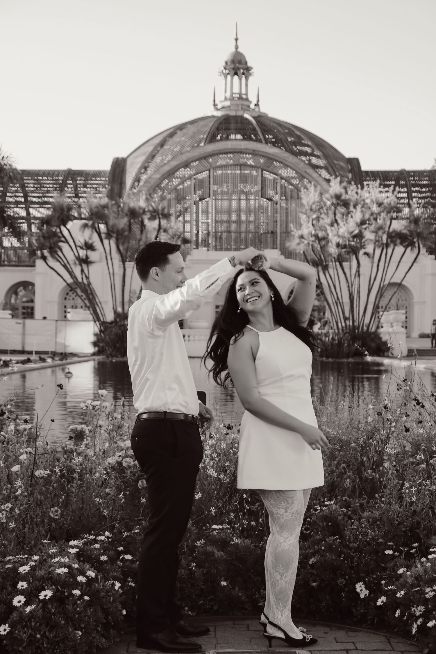 A black and white capture of a dancing moment in front of a historic glass conservatory.