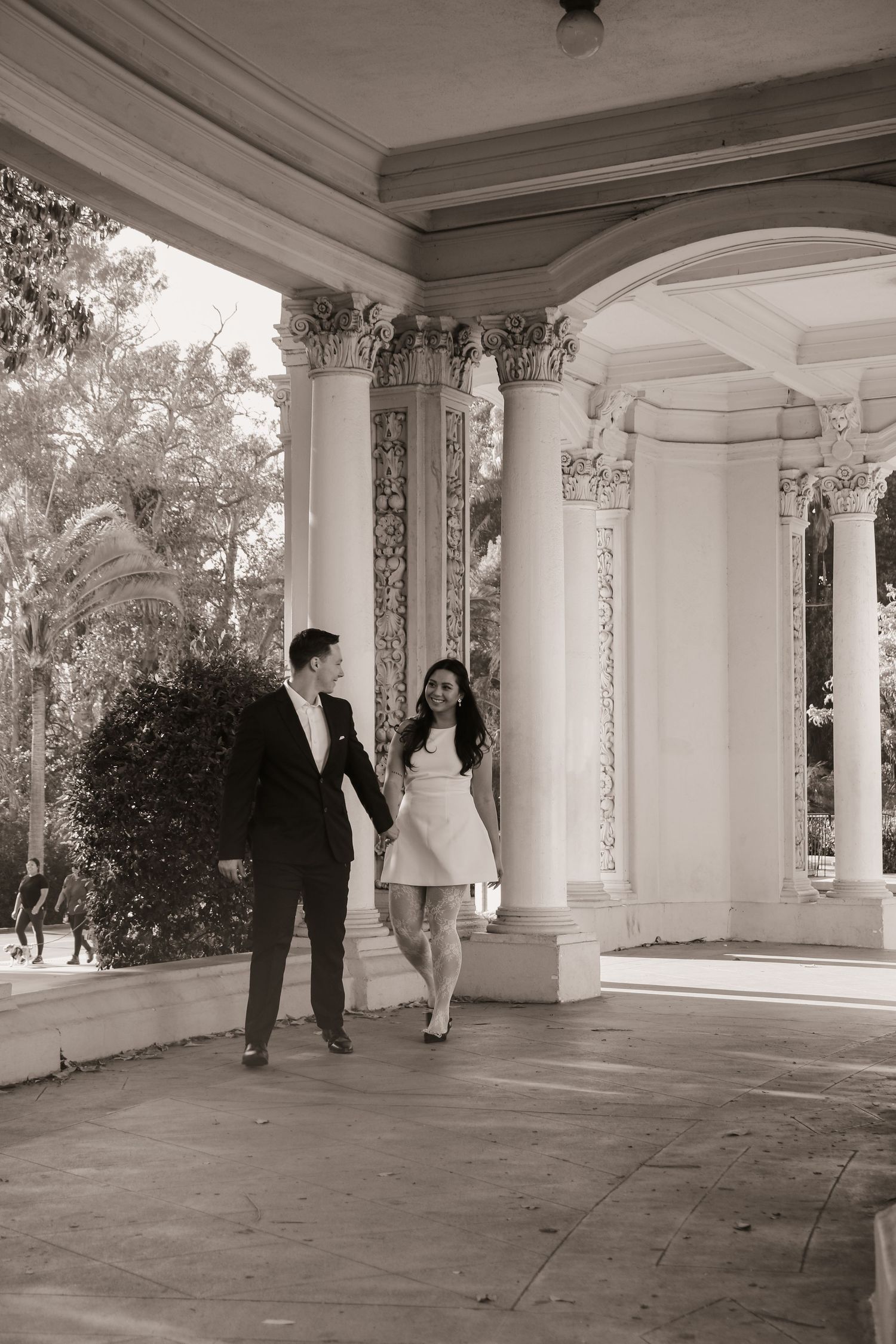 A couple shares candid moments under ornate columns and archways of a classical outdoor pavilion.