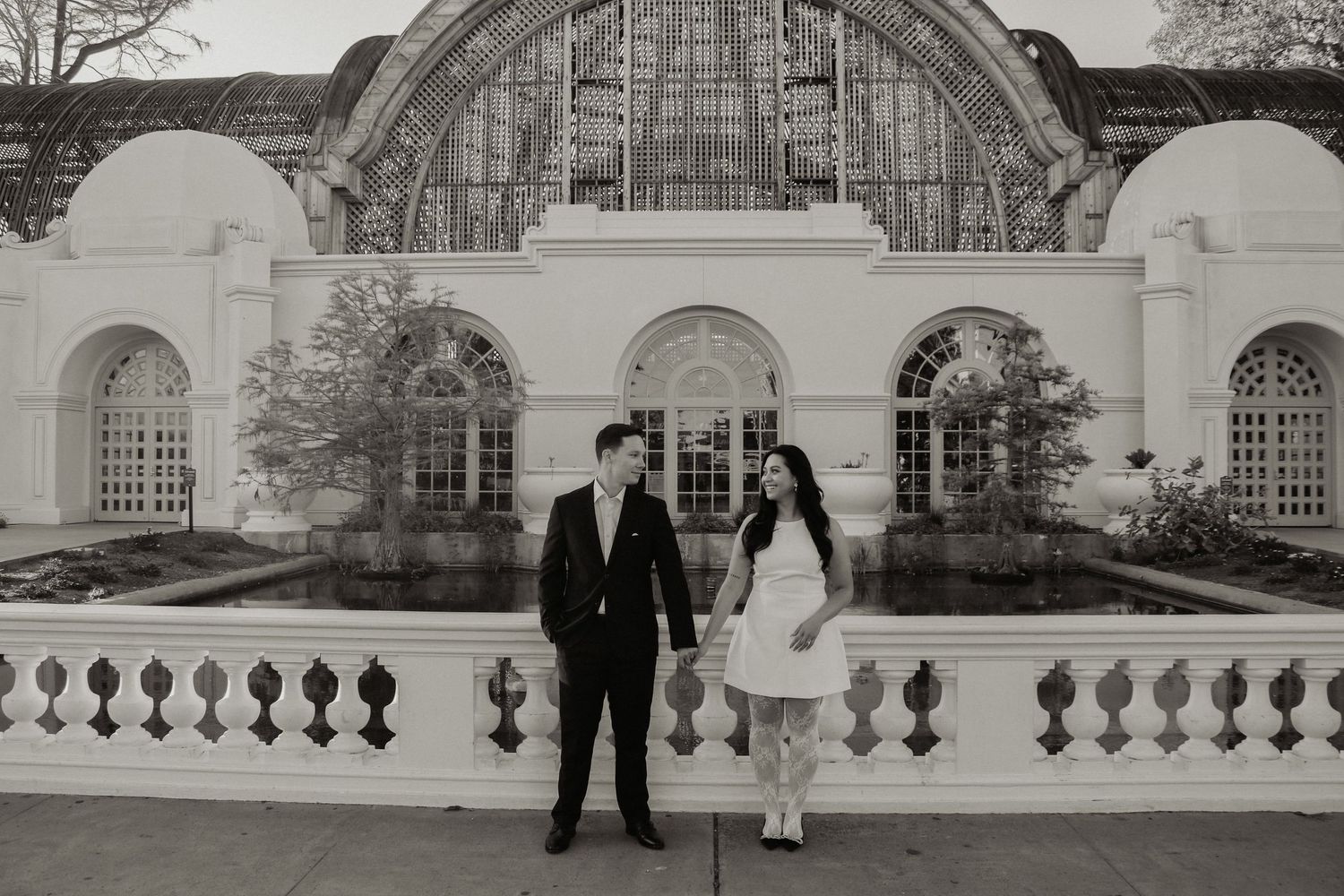 Black and white photo of couple standing by elegant stone balustrade at historic building entrance.