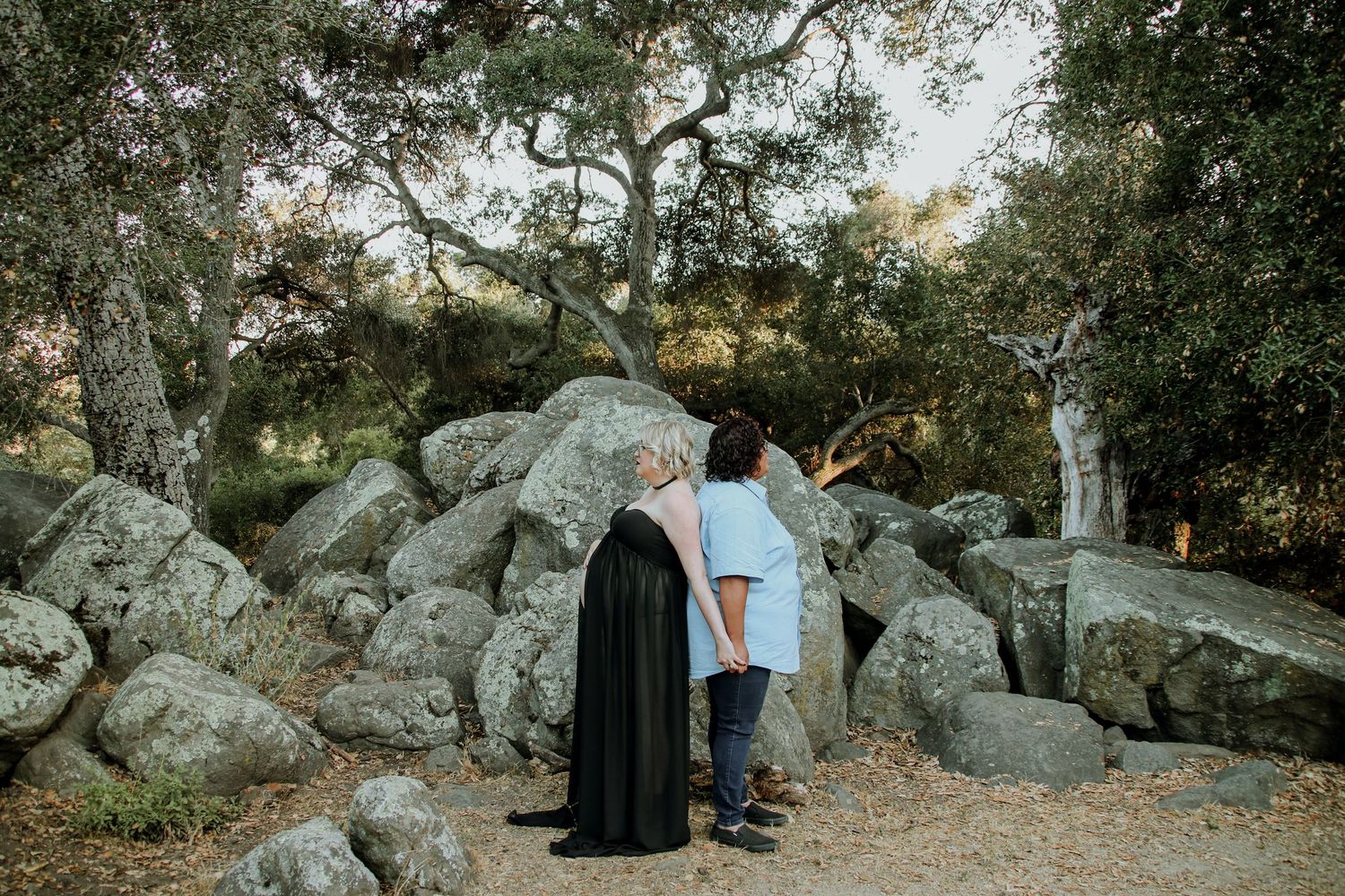 People gathered among large boulders in a natural wooded setting during golden hour.
