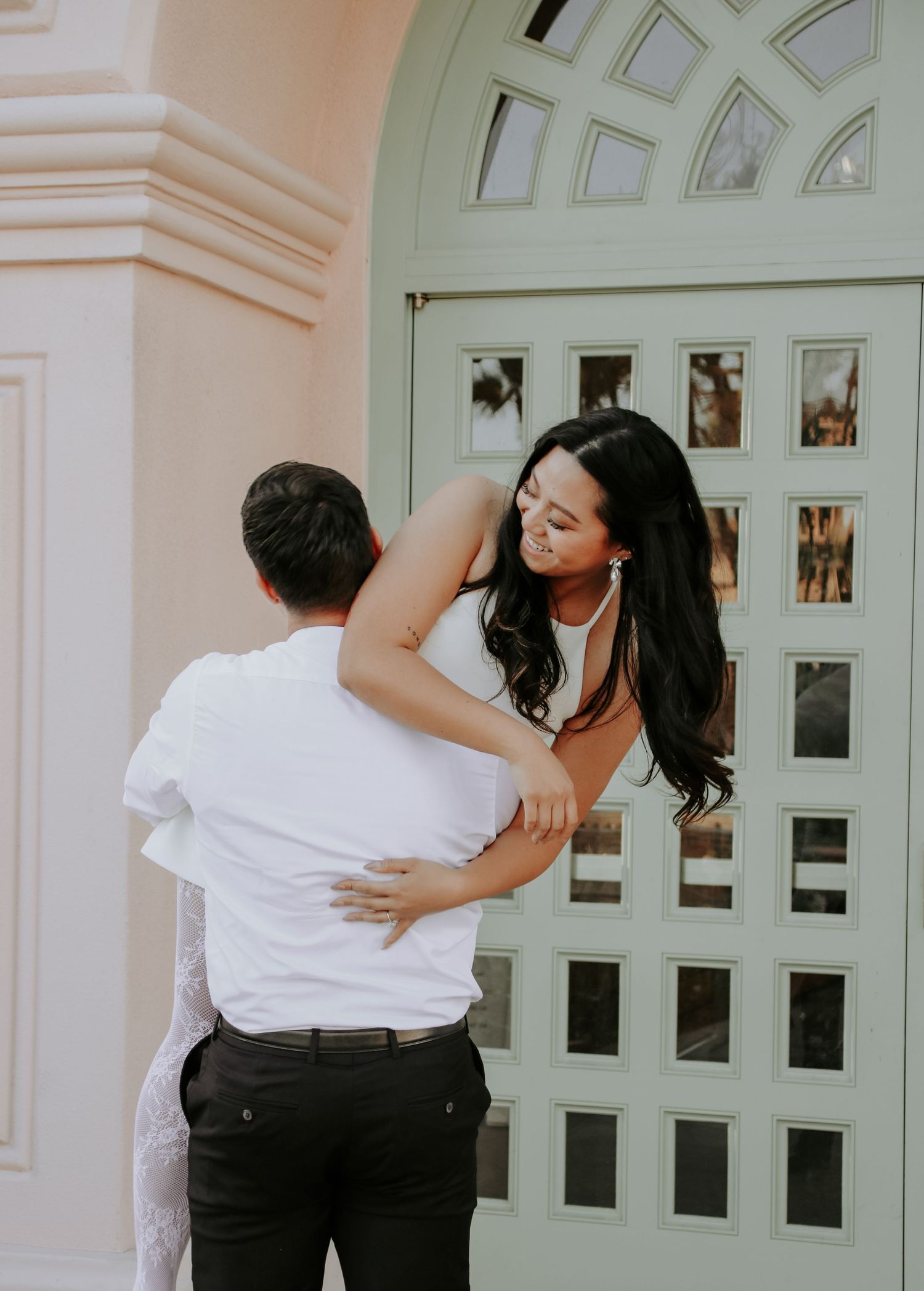 A romantic couple shares an intimate embrace in front of an elegant arched doorway.
