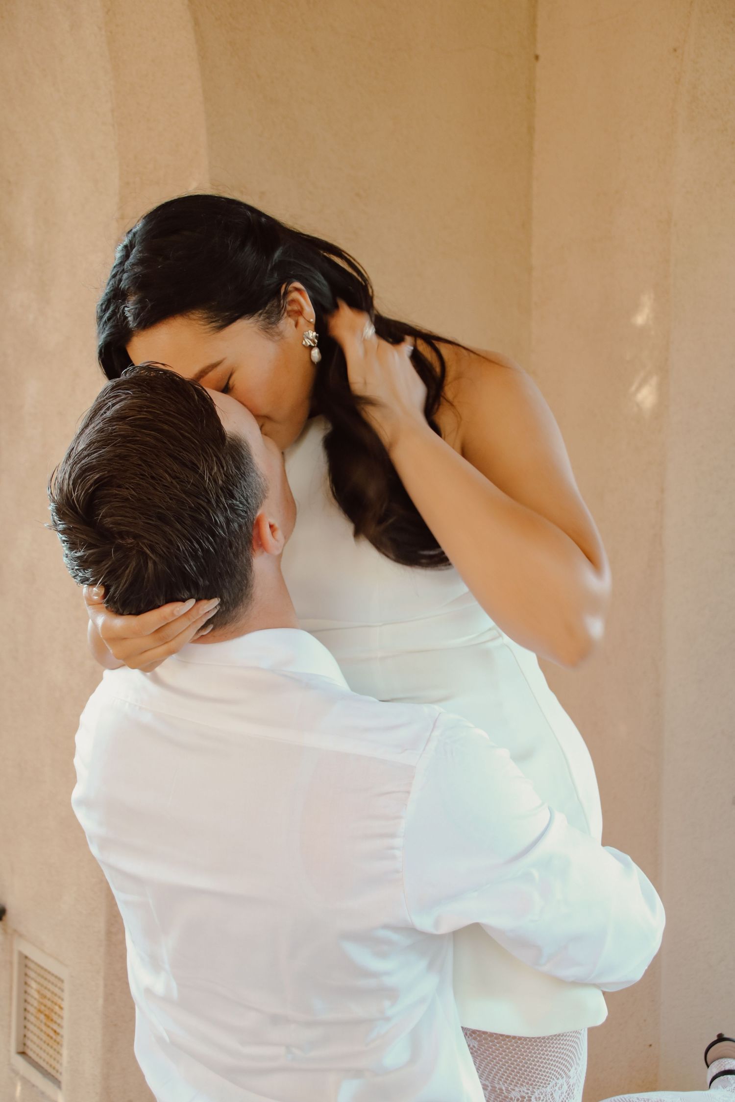 Couple embracing in soft natural light against neutral wall backdrop.