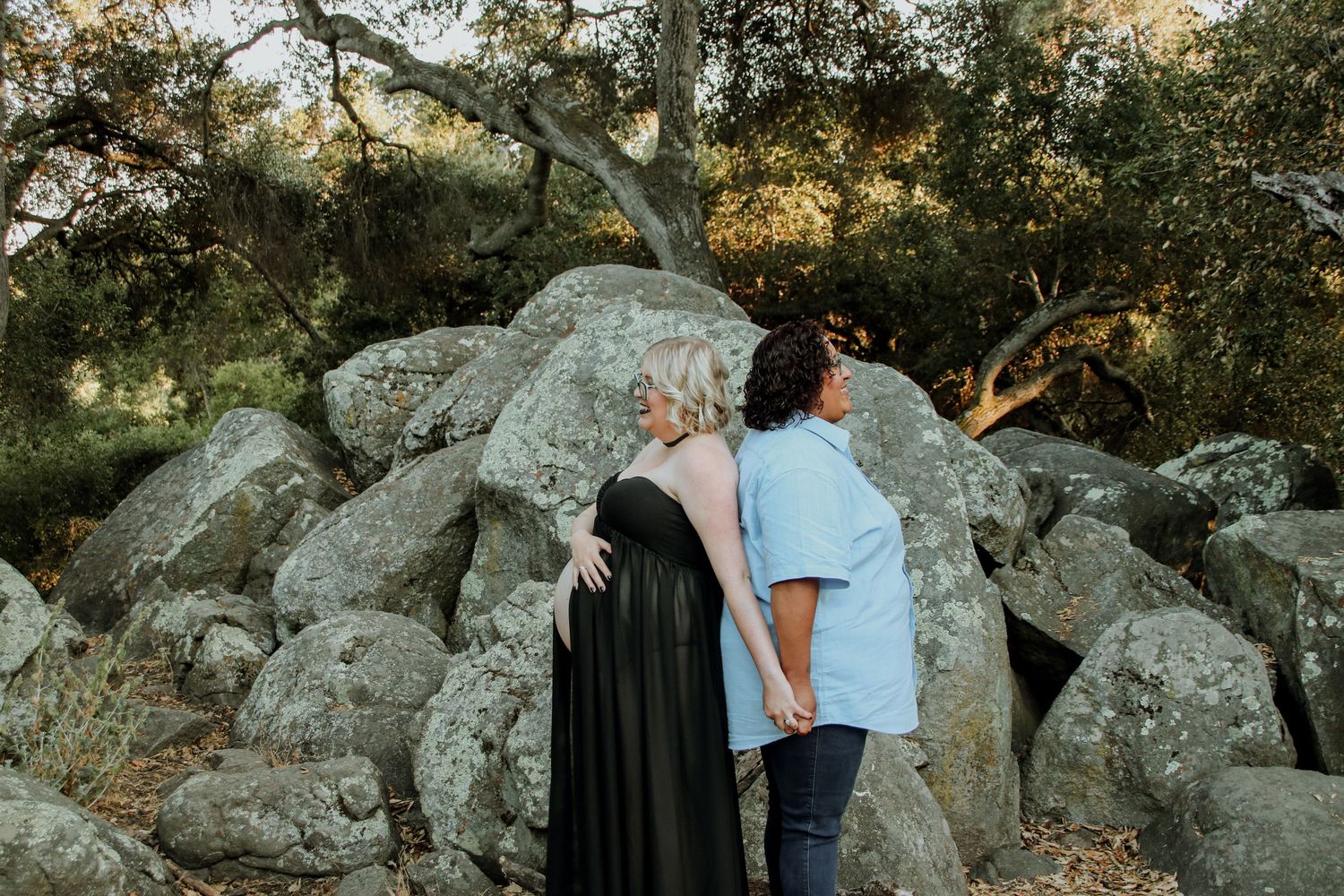A romantic couple poses on rugged granite rocks surrounded by trees during golden hour.