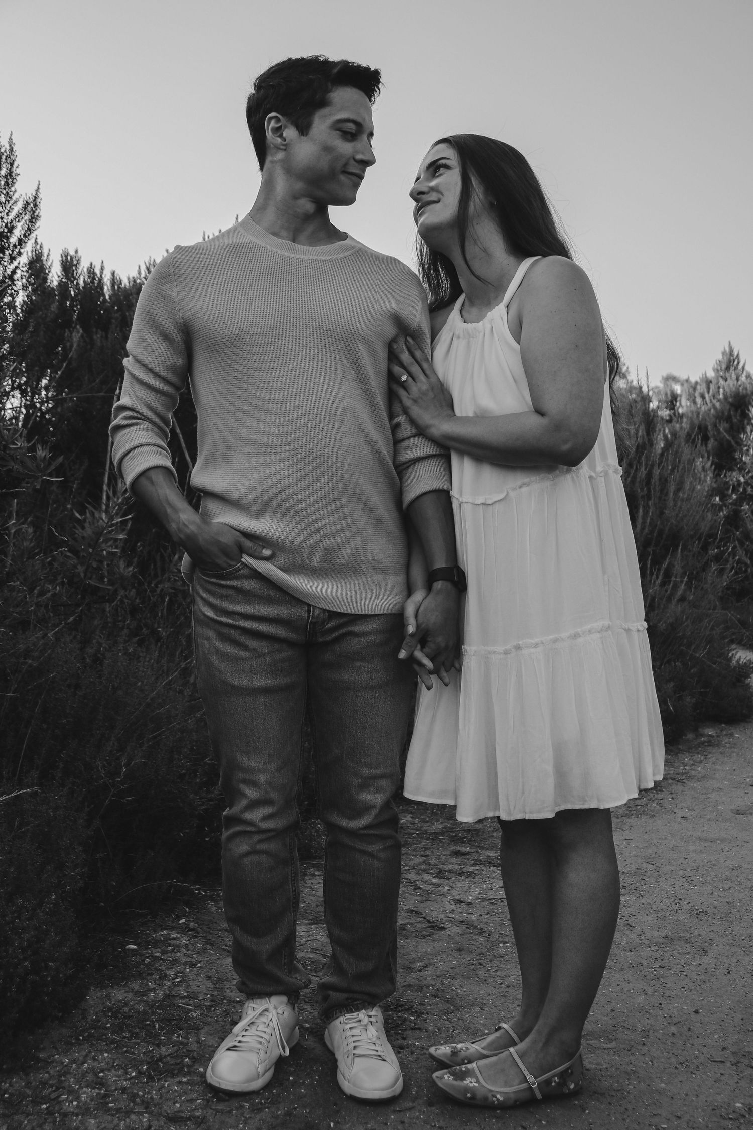 Black and white portrait of couple in casual wear on dirt path.