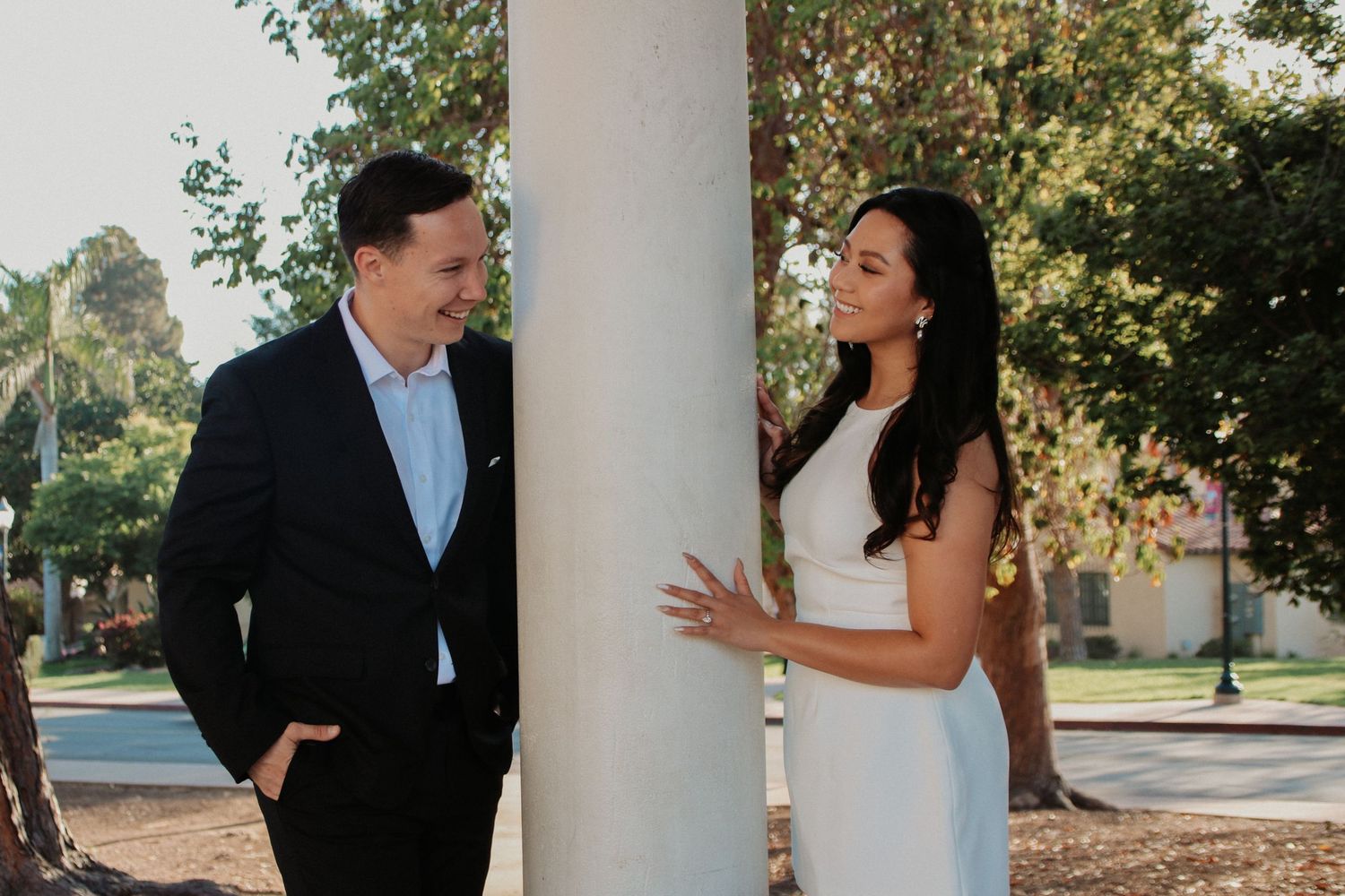 A couple chats beside a white column with trees visible in the background.