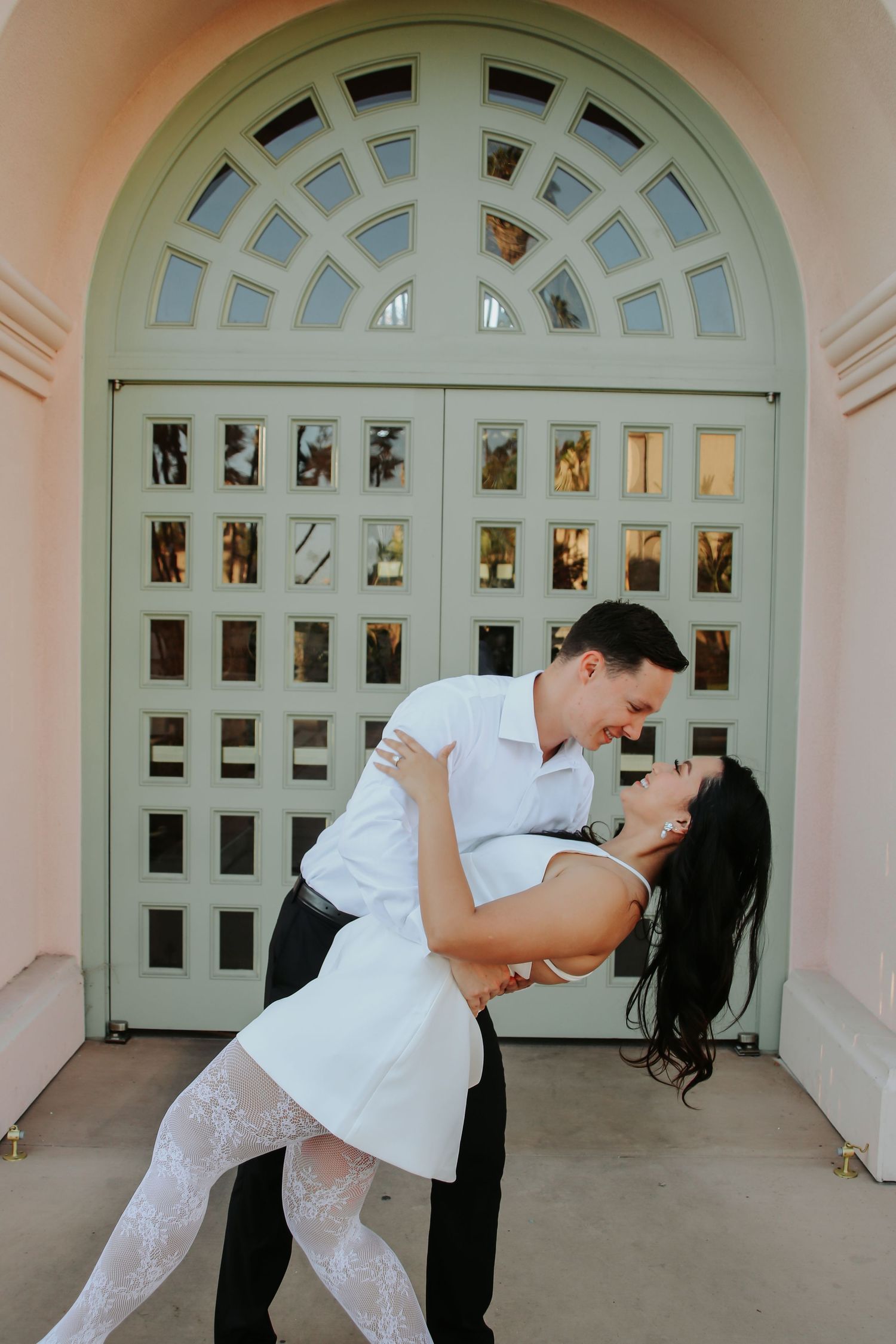 A romantic dip pose in front of an elegant arched doorway with a latticed design.