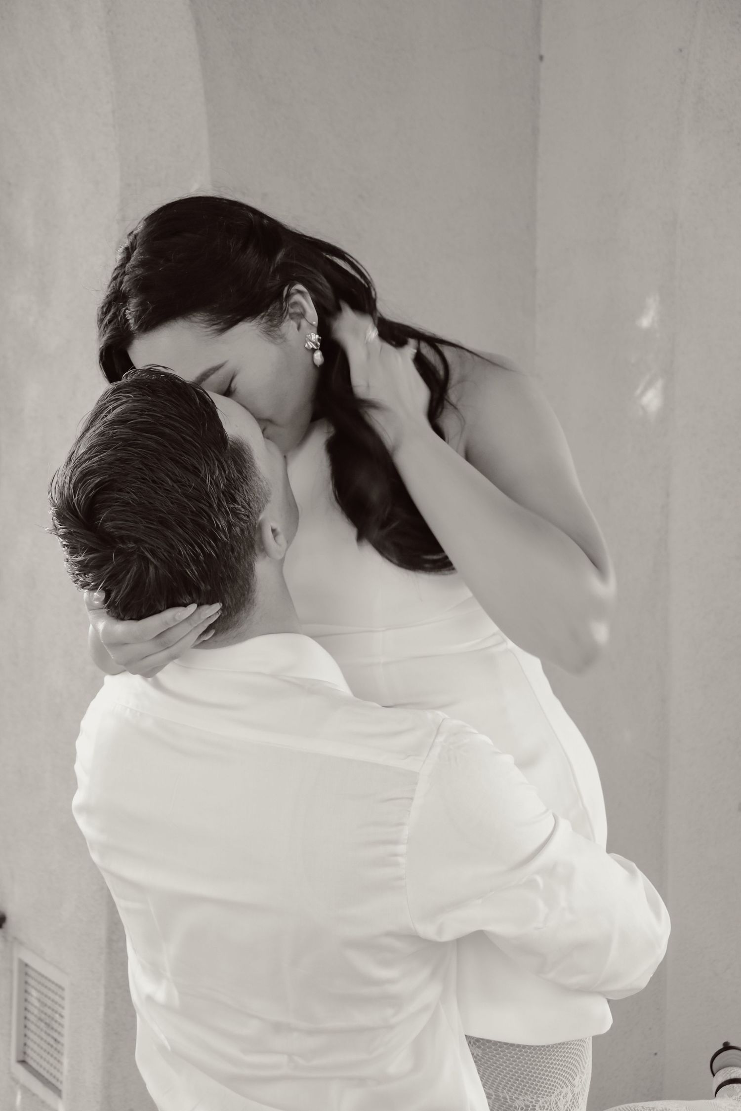 Romantic black and white portrait of couple sharing intimate moment against wall.
