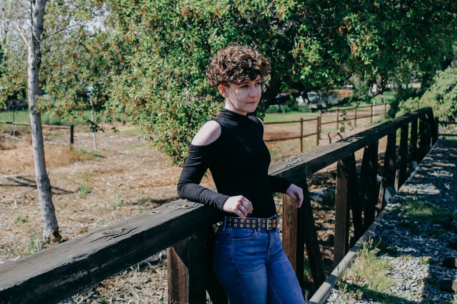 Person balancing and walking playfully along wooden railroad tracks surrounded by trees in a park setting.