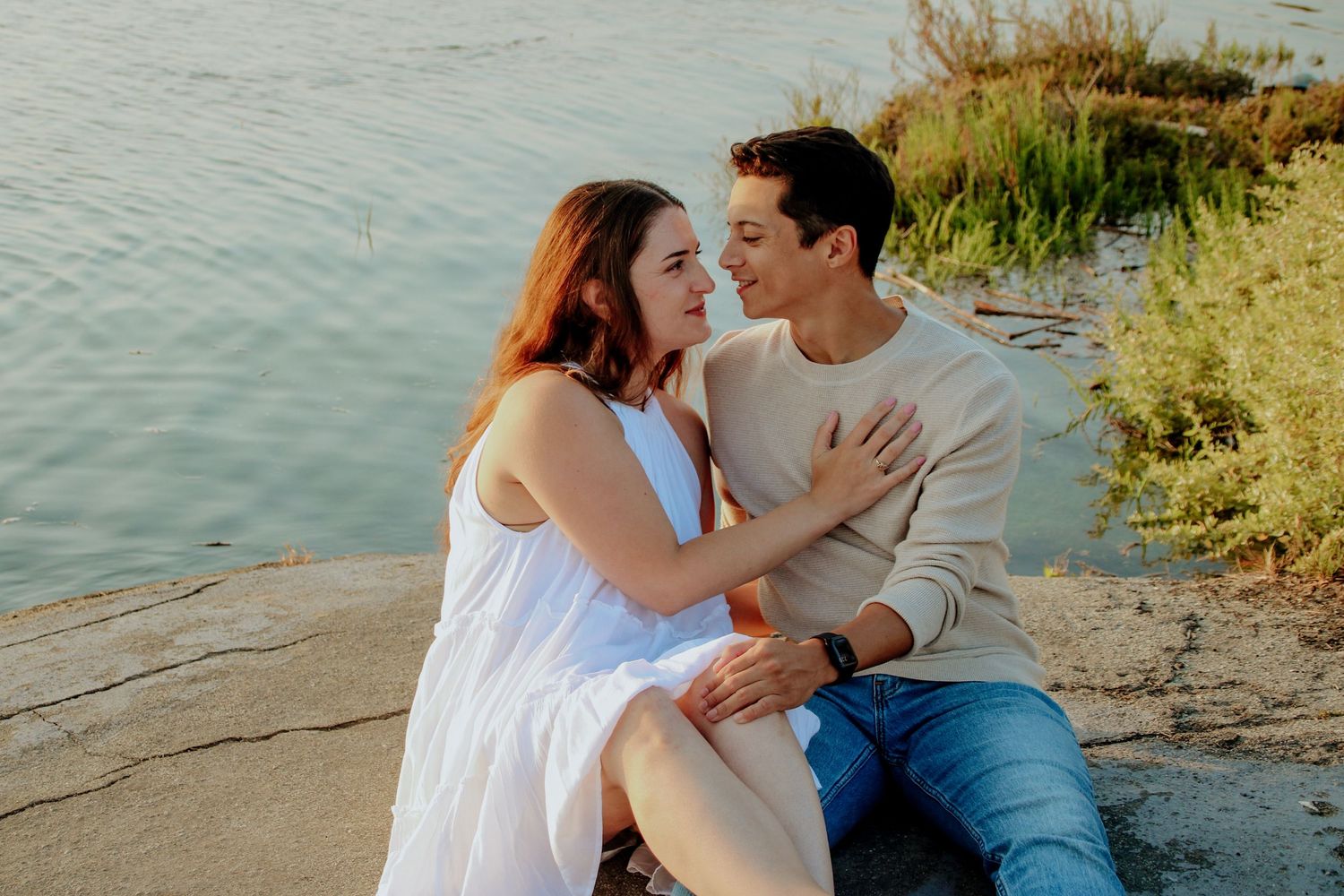 Couple in coordinated outfits sharing intimate moment on rocky waterfront during golden hour.