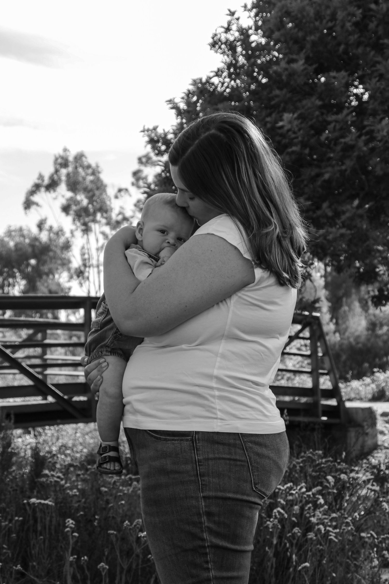 Black and white portrait of mother and infant sharing intimate moment in garden setting.