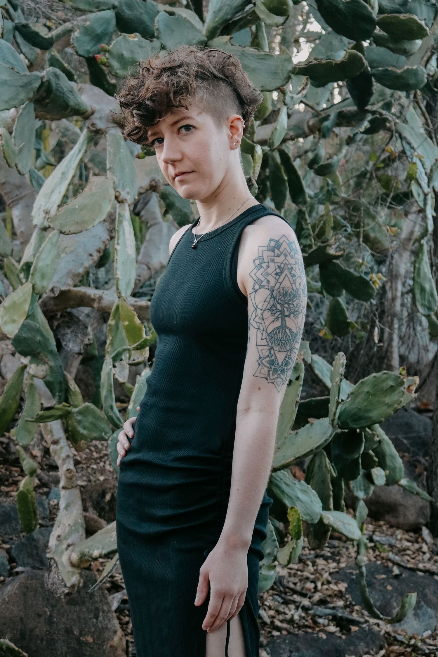 Fashion photo among desert flora showing sleek black dress and artistic arm tattoo.