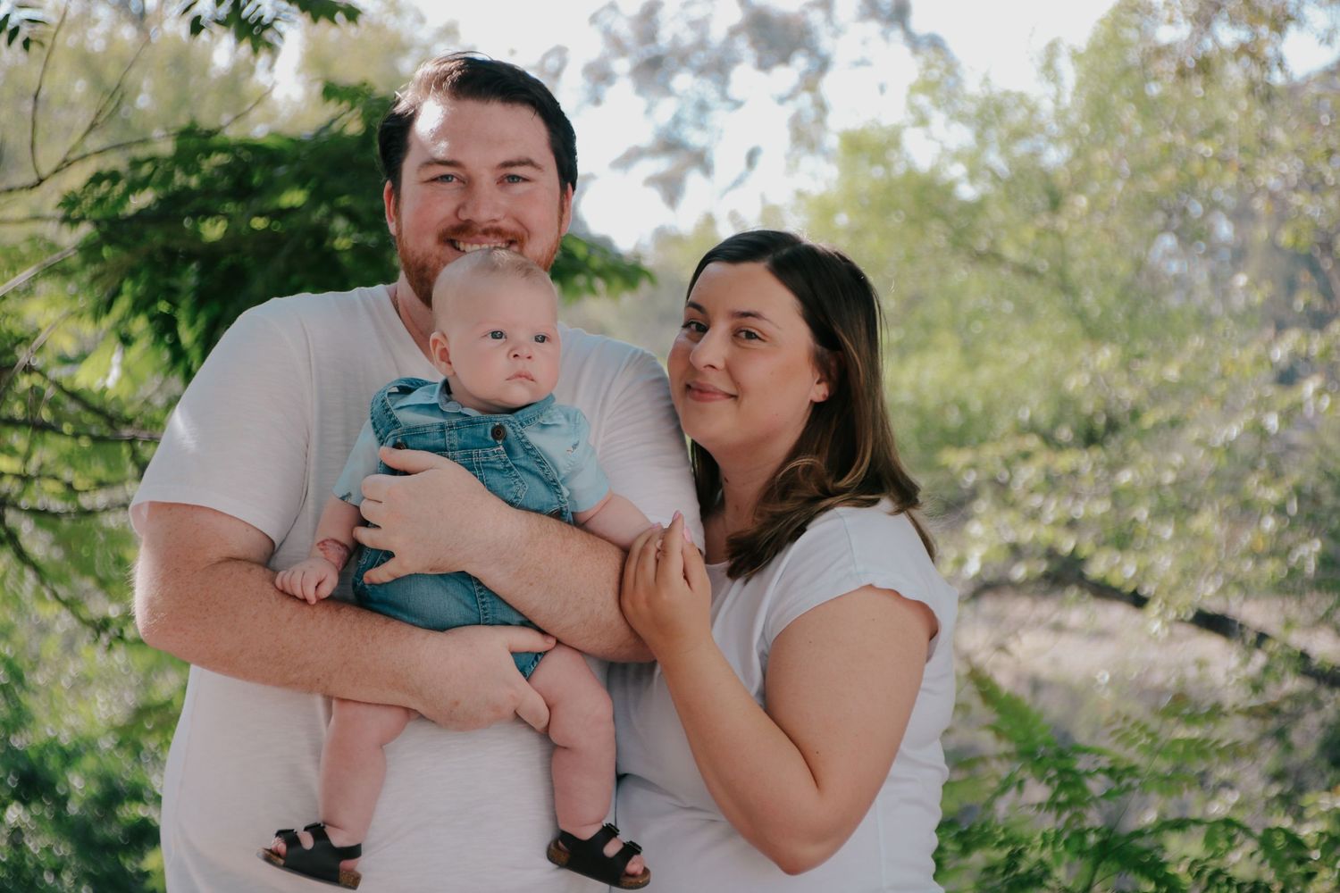 A sunlit family portrait capturing genuine smiles and interactions in a lush outdoor setting.