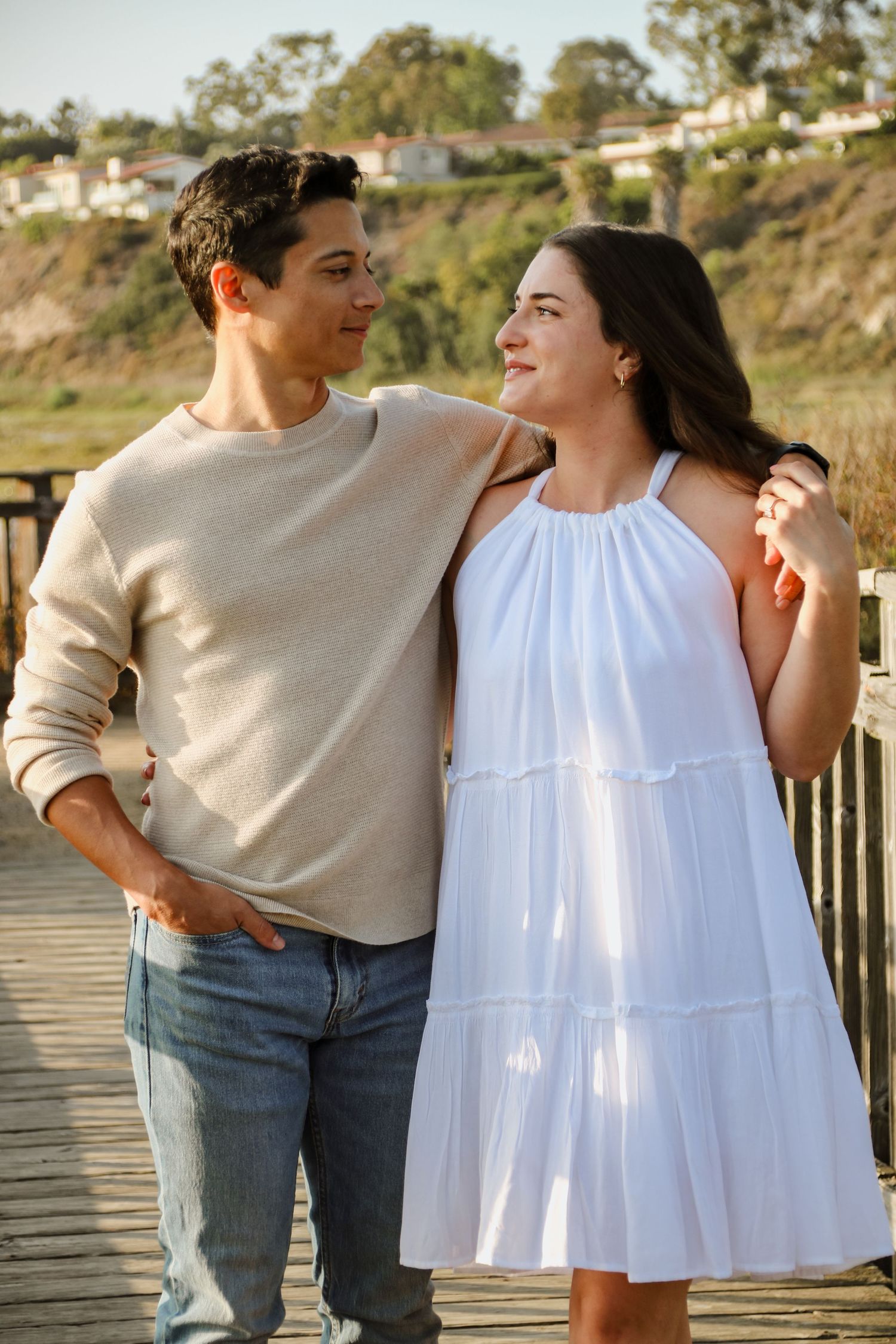 Couple in casual attire sharing intimate moments on a wooden boardwalk by the ocean.