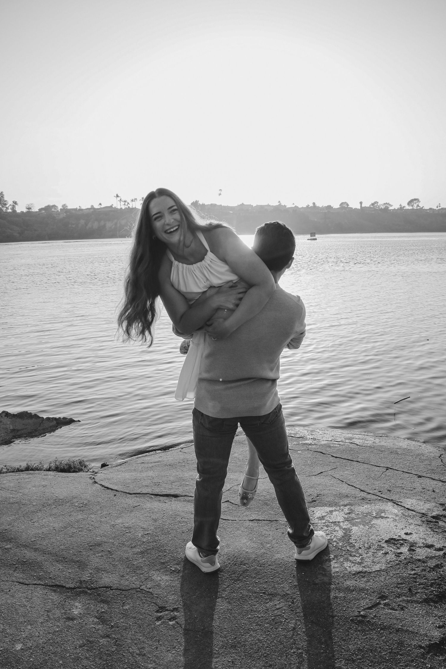 A romantic couple sharing a playful moment by the waterfront during sunset.