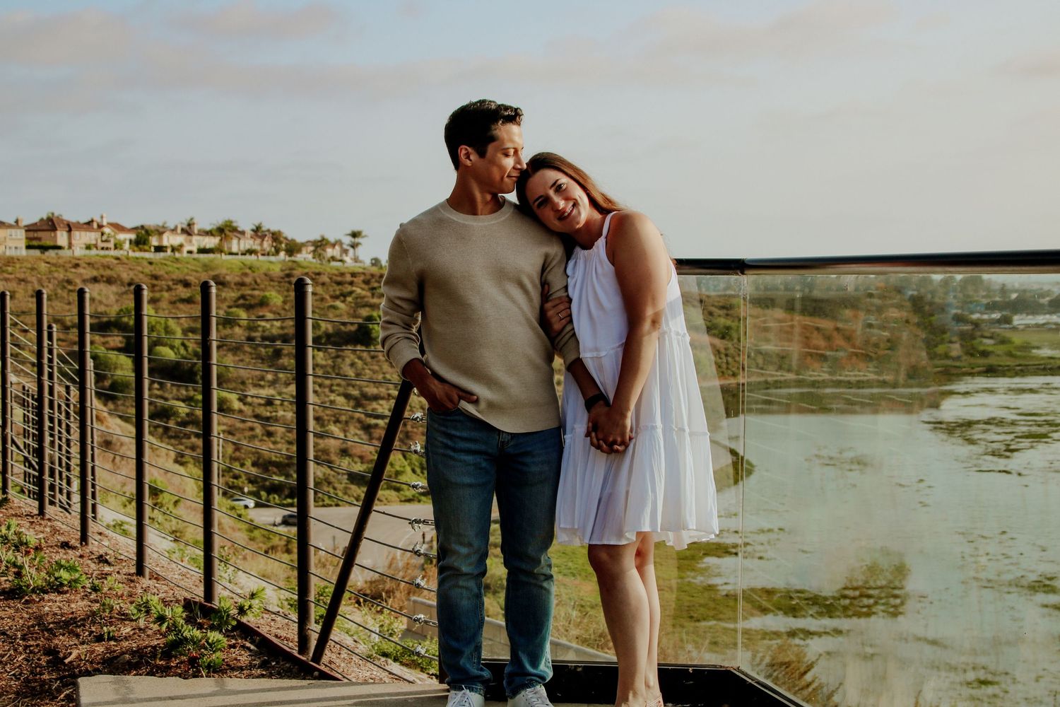A romantic couple poses together on an elevated deck with scenic marsh views during golden hour.