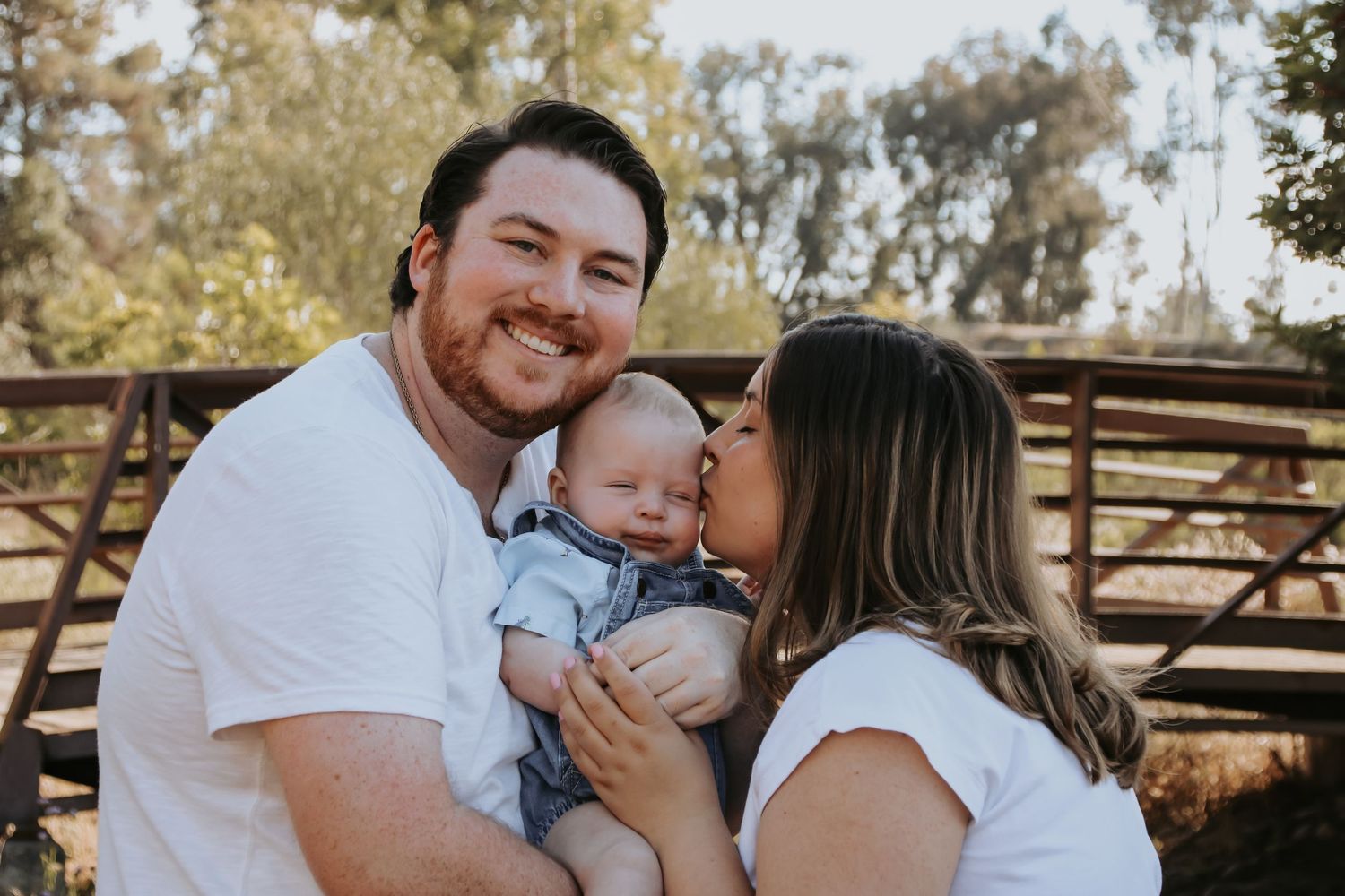 Family shares tender moments together in an outdoor setting with rustic wooden fence backdrop.