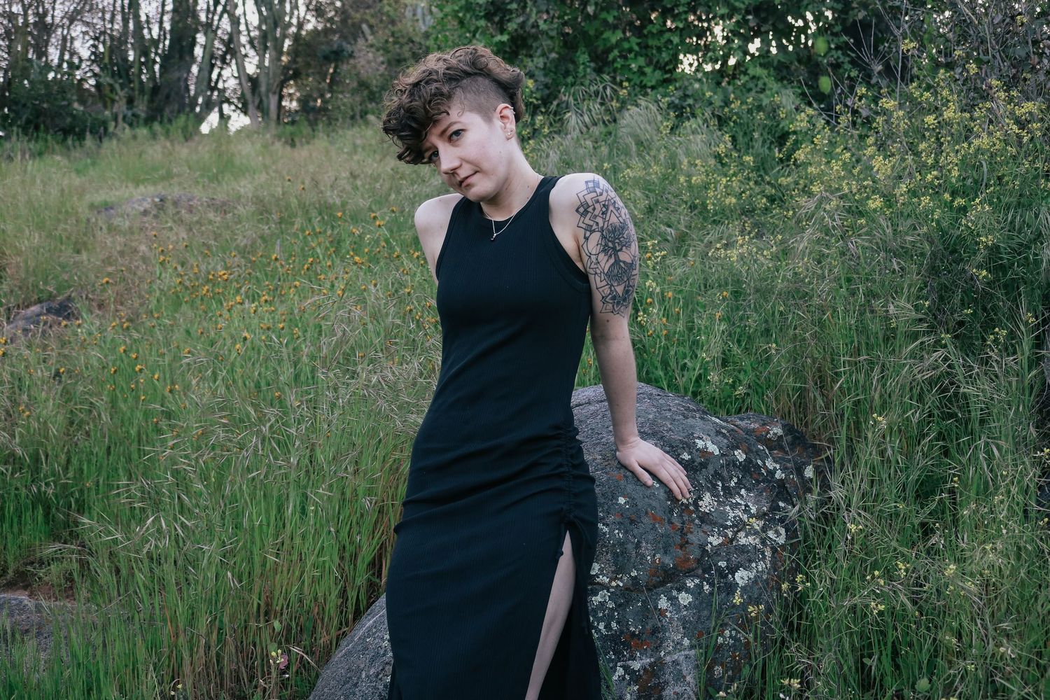 Person in black dress sits on rocky outcrop surrounded by greenery.