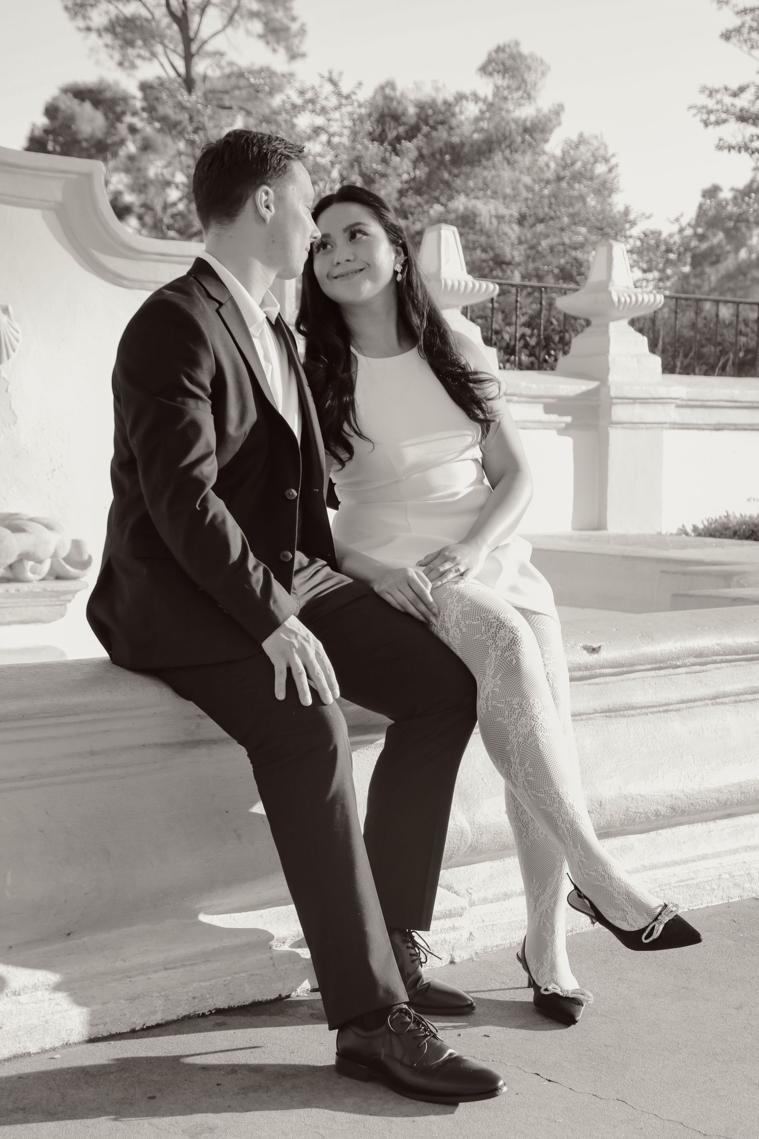 Couple in formal attire sharing an intimate moment while sitting on stone steps outdoors.