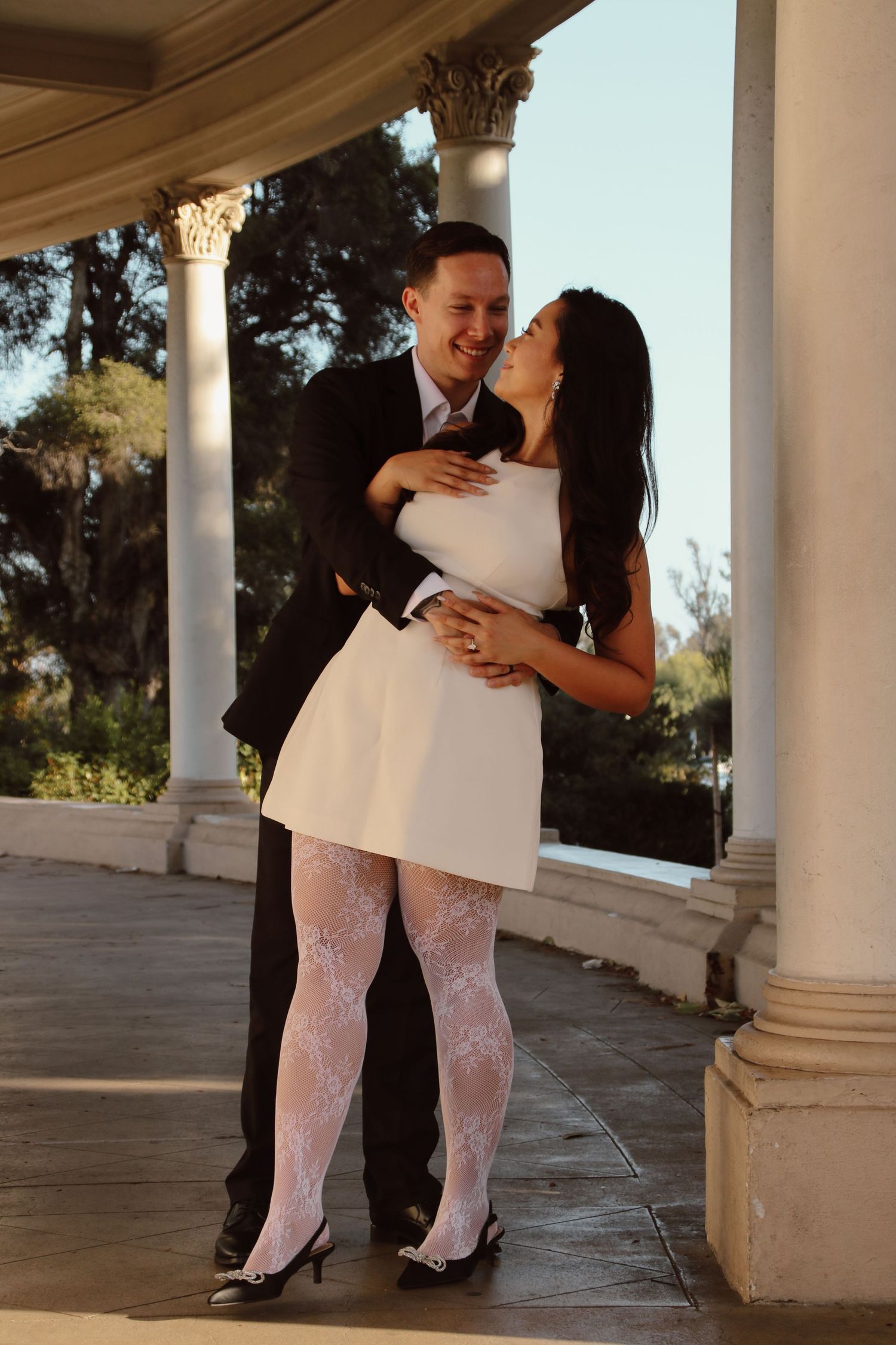 A couple embraces romantically under a colonnade with ornate architectural details.