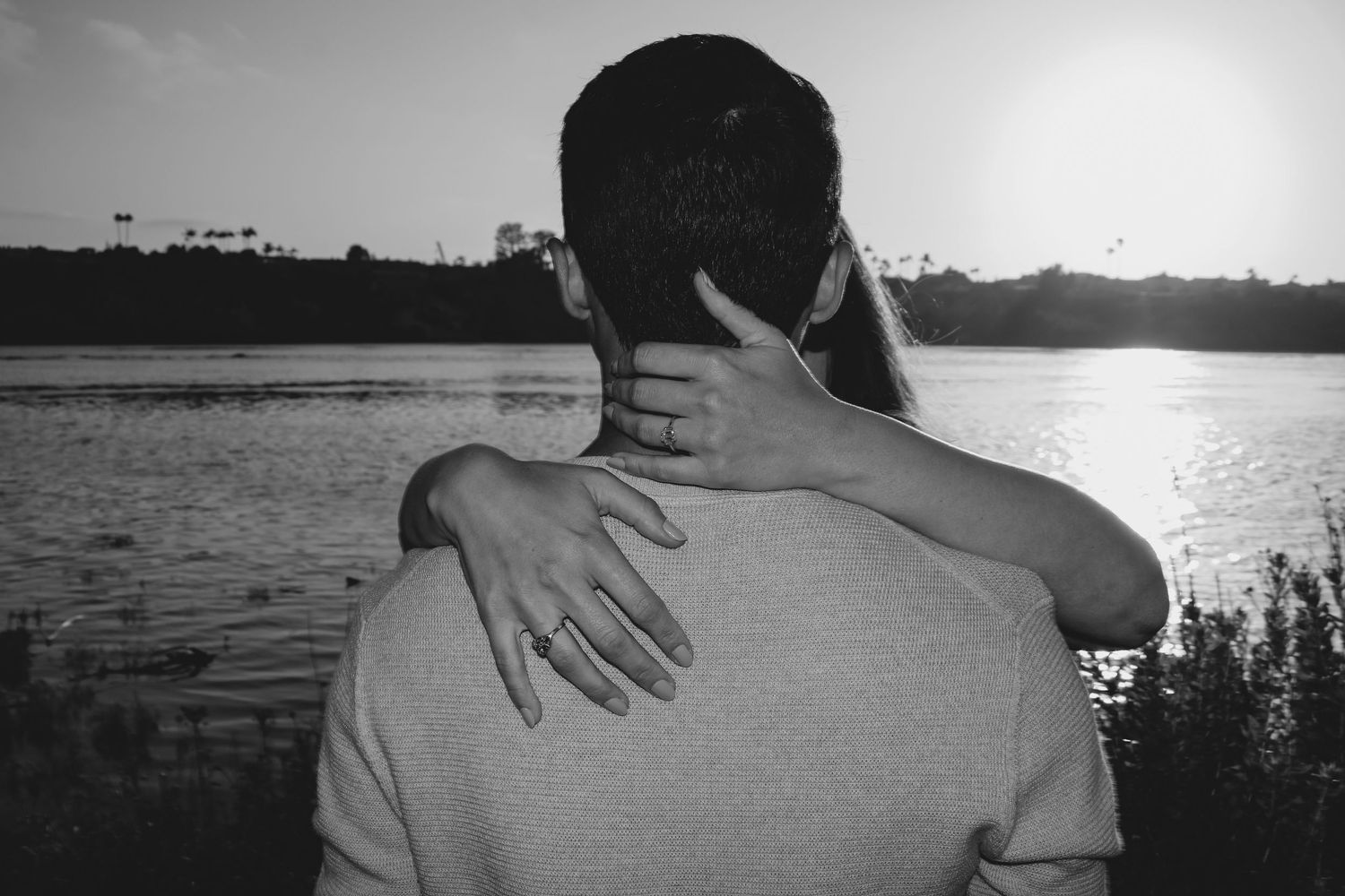 Silhouette of a tender embrace against a sunset waterfront landscape.