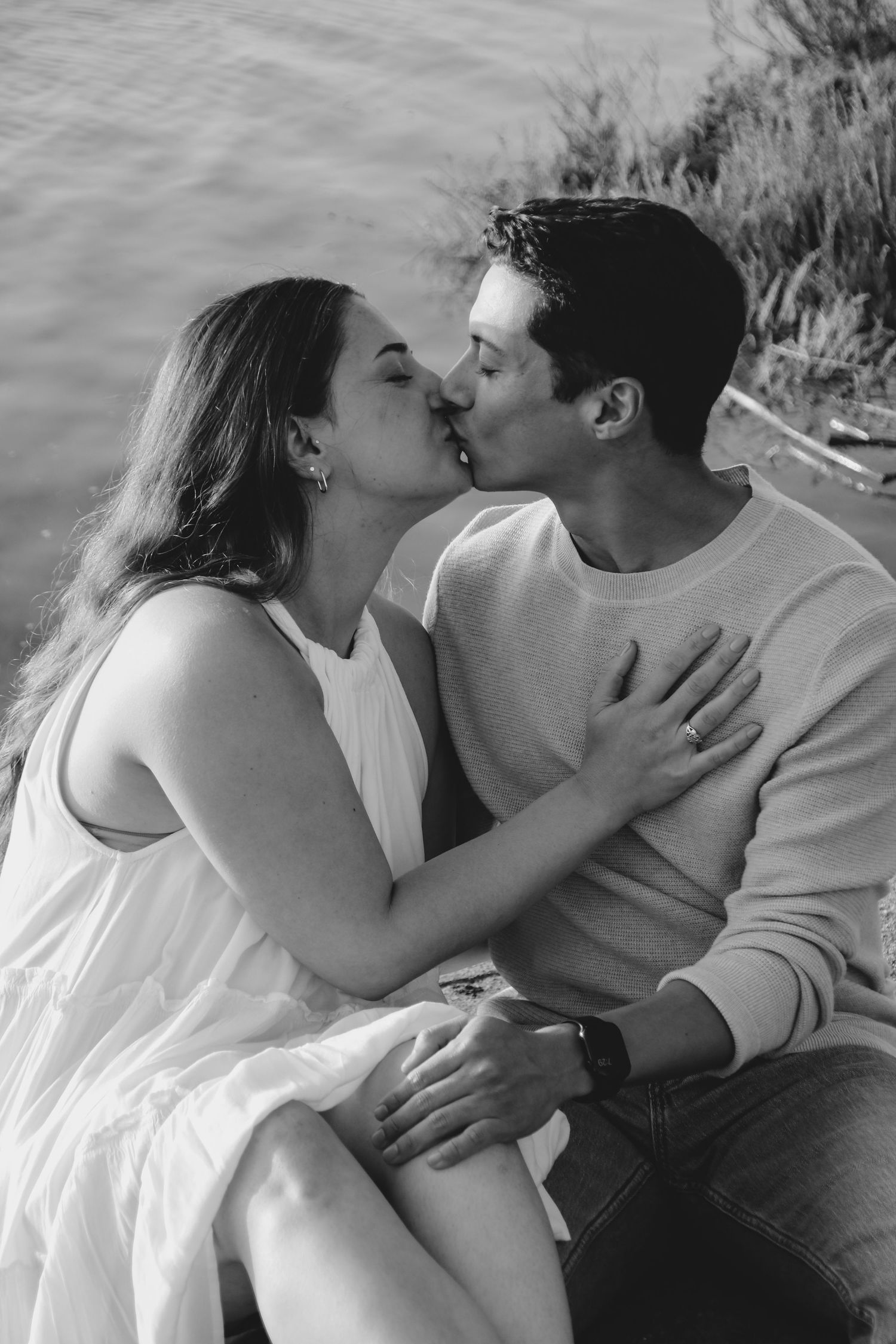 Intimate black and white photo of couple kissing by waterfront.