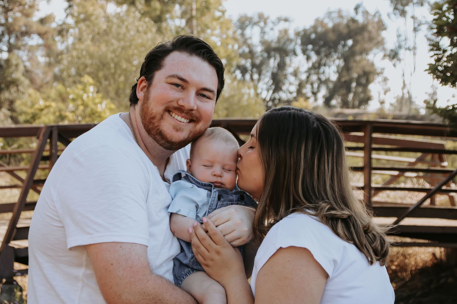 Family shares tender moments together in an outdoor setting with rustic wooden fence backdrop.