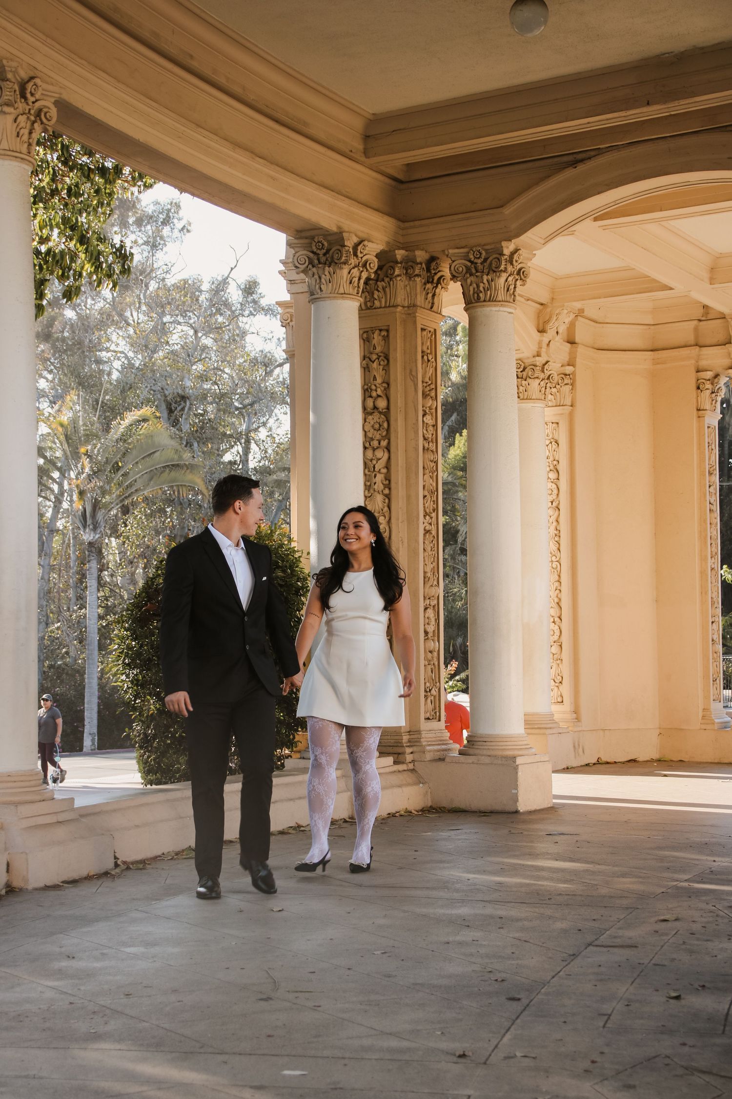 Couple enjoying a fun photoshoot moment under decorative pillars of a beautiful outdoor portico.