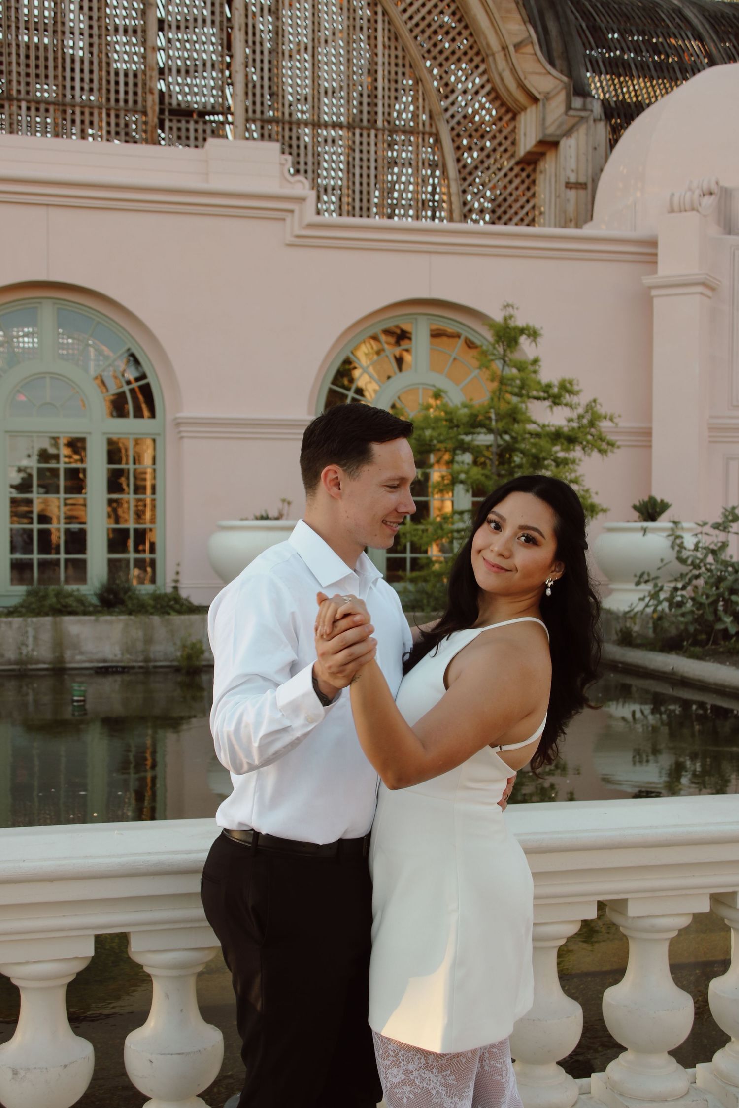 Elegant couple dancing together against backdrop of ornate architecture and reflecting pool.