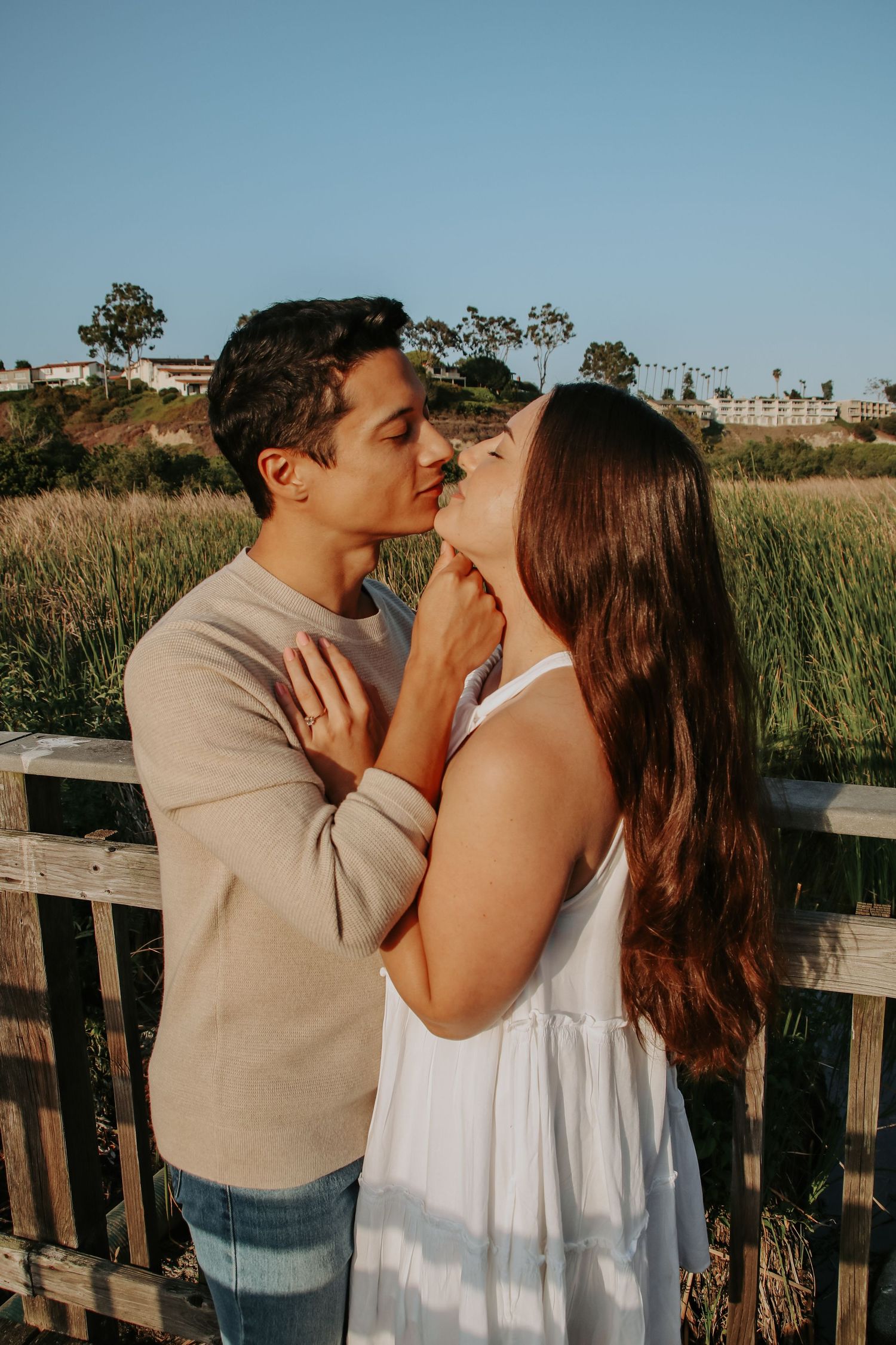 Couple in coordinated outfits sharing tender moment against coastal background.