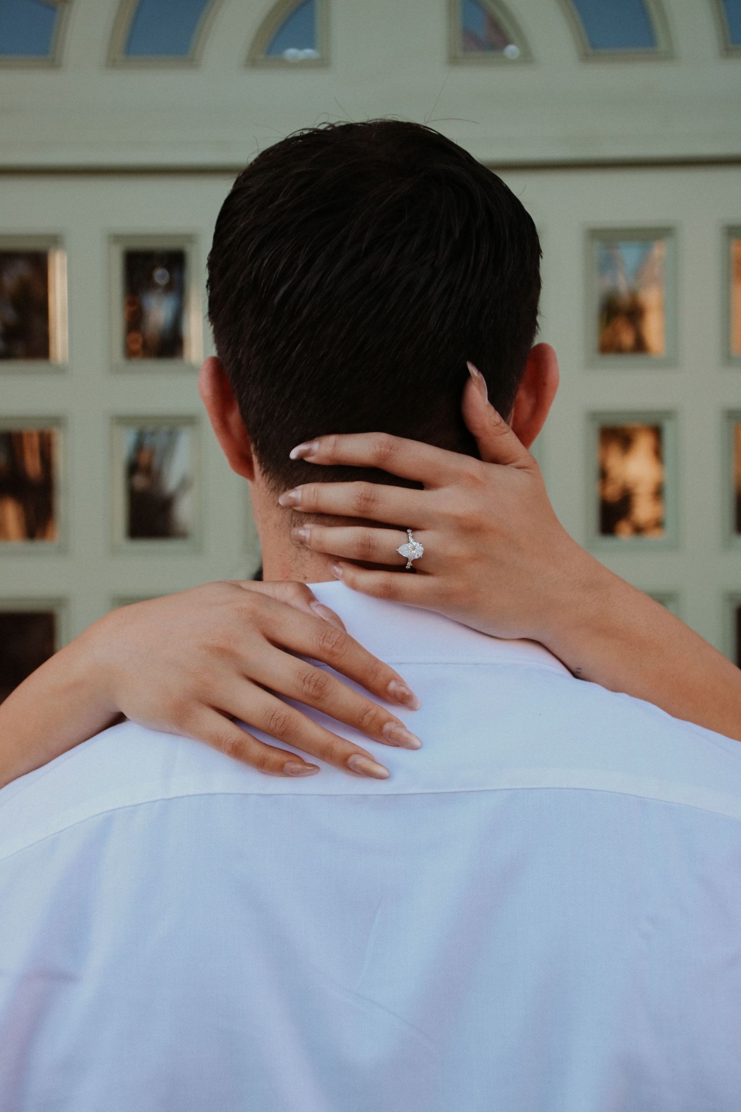 Close-up of hands embracing with an engagement ring visible against a white shirt.
