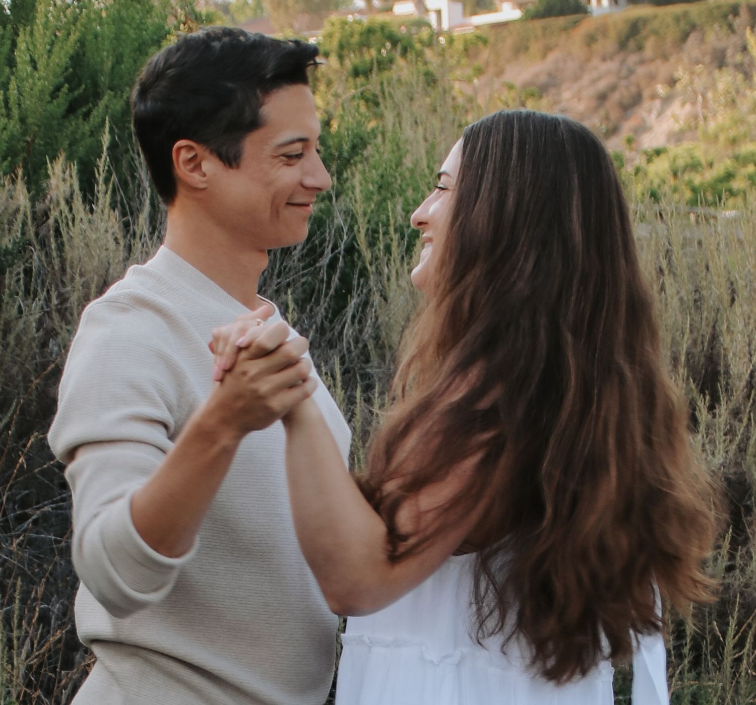 A couple shares a romantic dance moment on a coastal trail during golden hour.