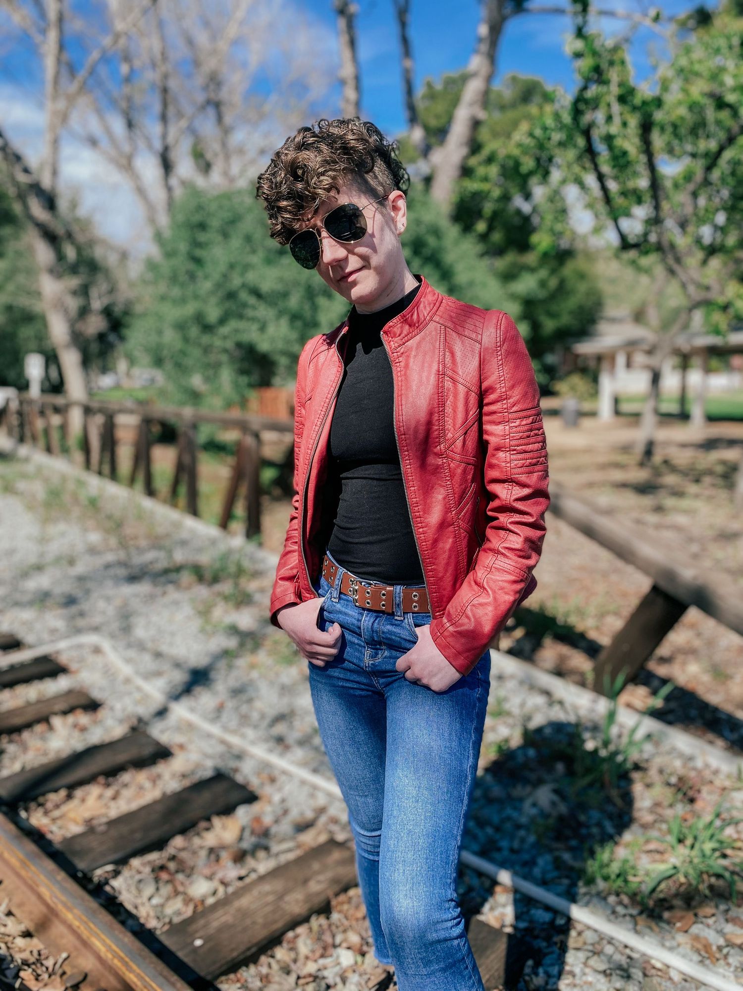 Stylish retro fashion photography featuring red leather jacket and blue jeans against rustic railroad tracks.