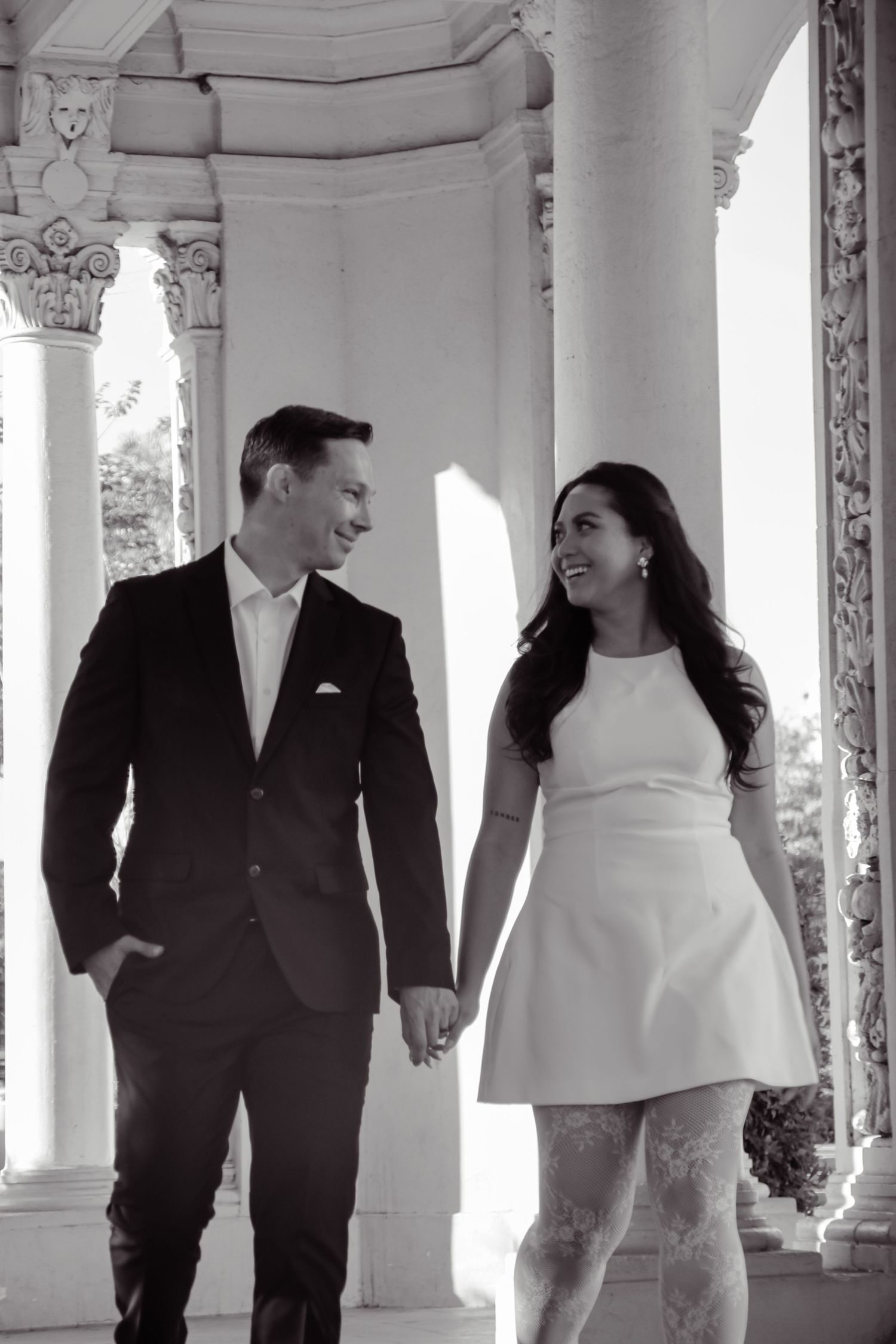 Happy couple in formal wear sharing a moment among classical columns in black and white.